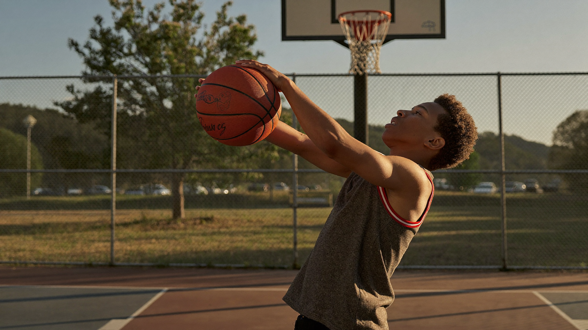 A teenage boy jumping to take a shot on an outdoor basketball court