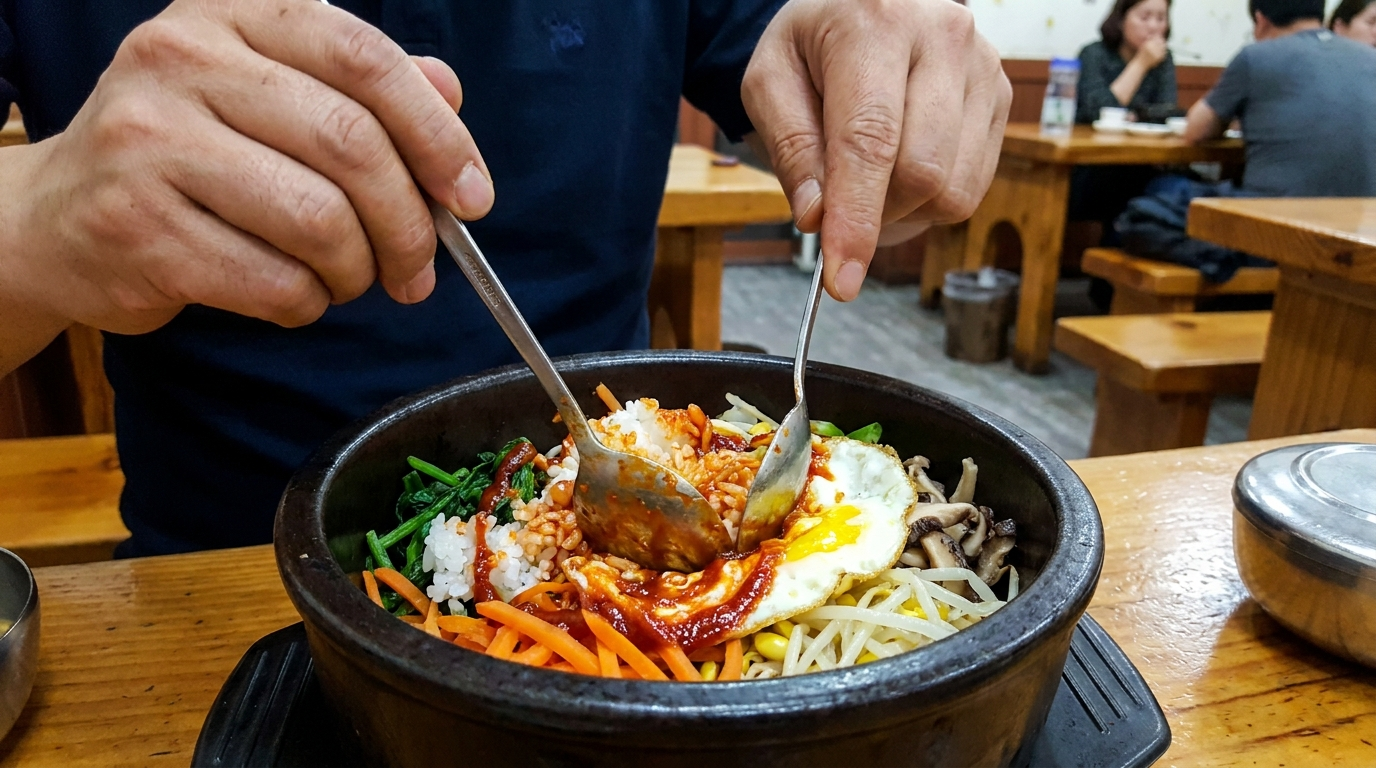 Hands mixing Korean bibimbap with a spoon and gochujang sauce