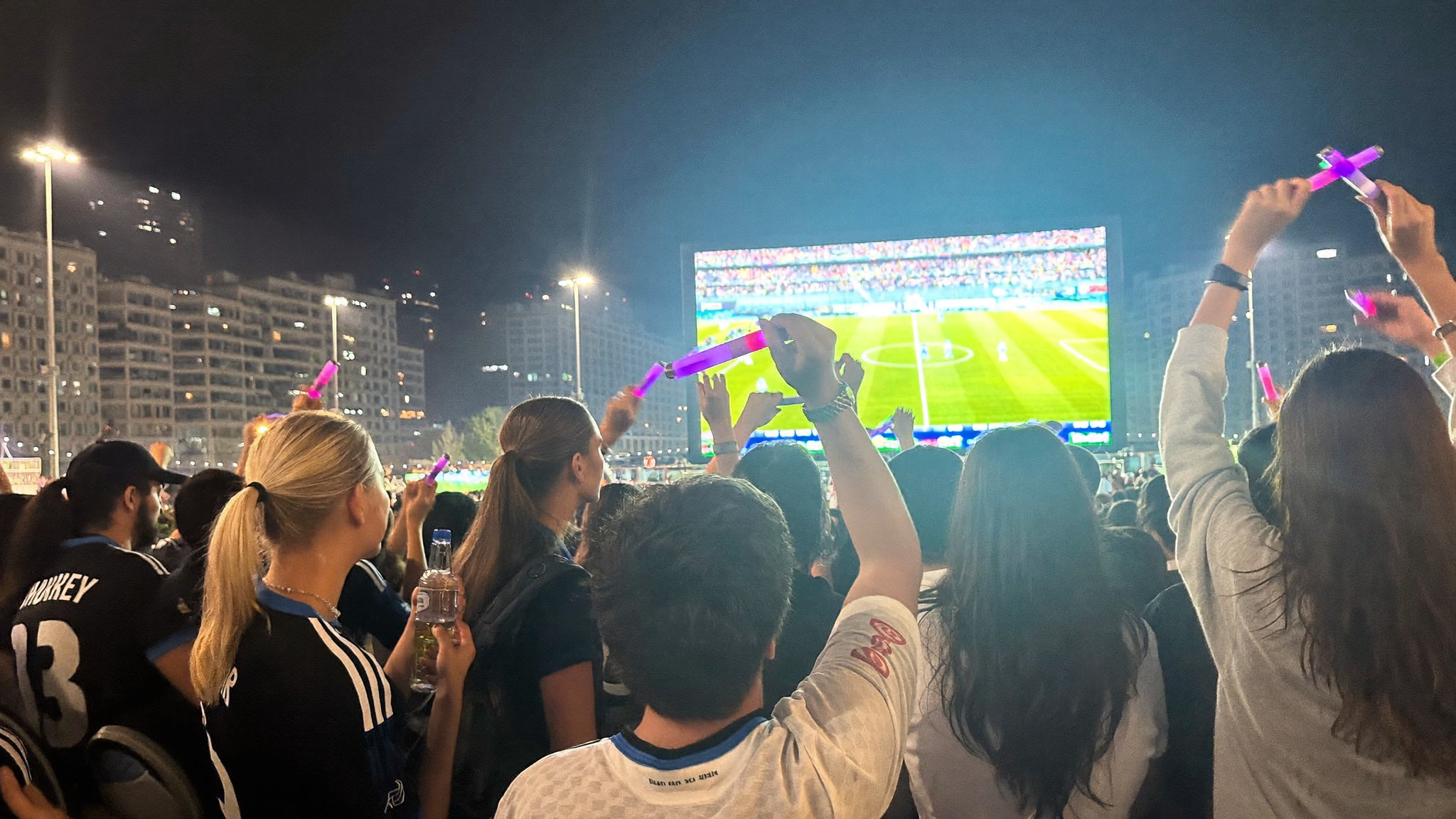 Fans watching World Cup 2026 final on an outdoor screen with purple K-pop light sticks