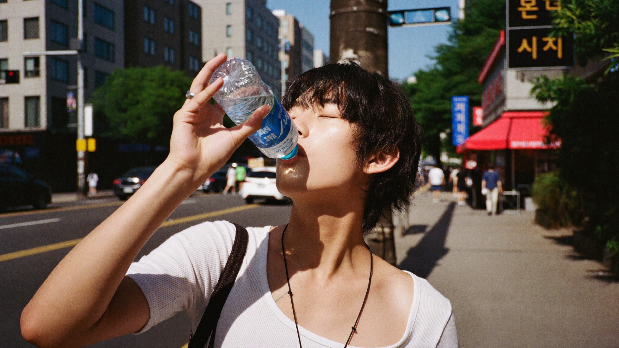 Tourist drinking free cold water from a Korean public vending machine on a hot Seoul street
