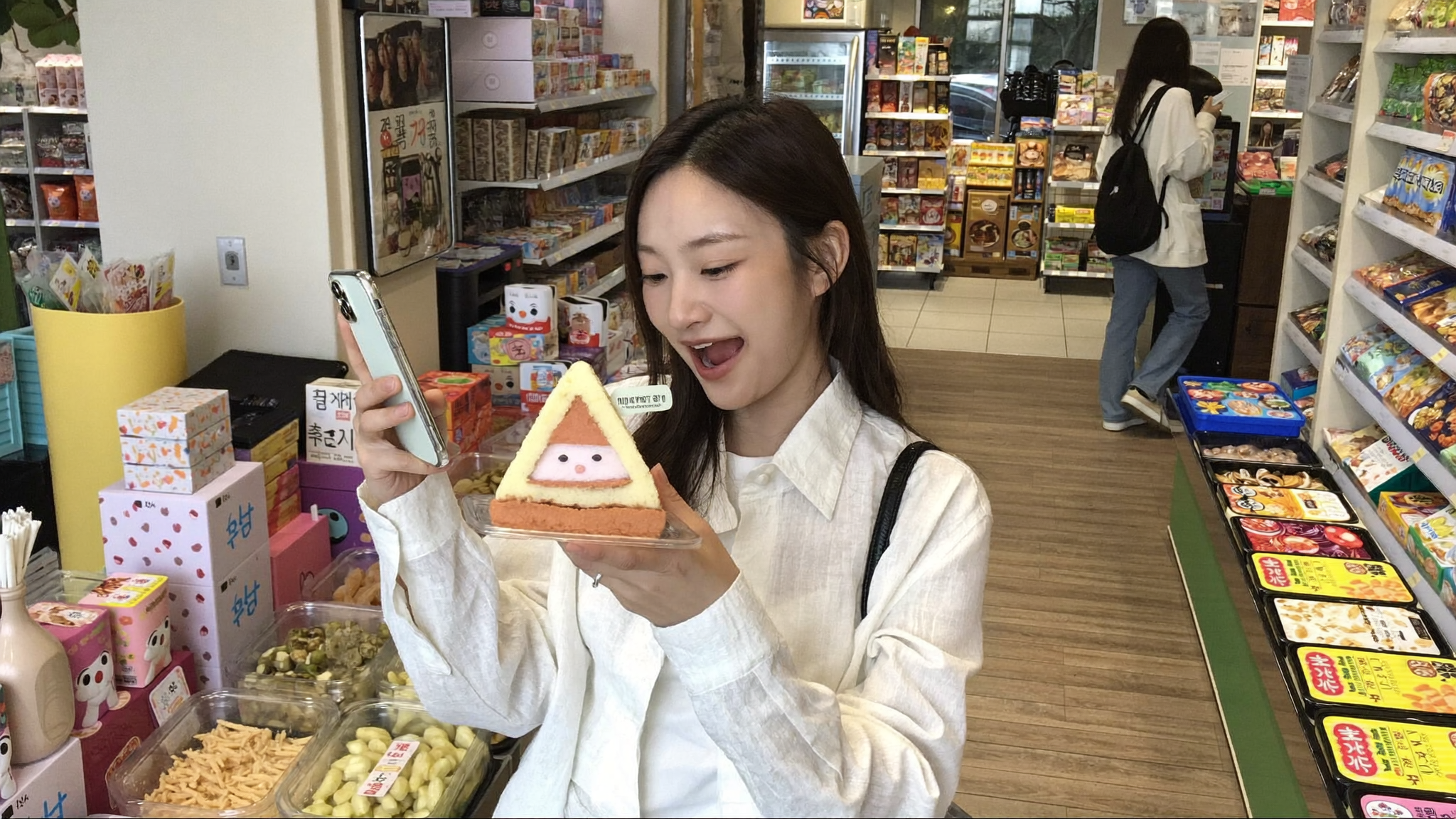Young woman excitedly holding a hyper-realism dessert shaped like triangle kimbap at a Korean convenience store