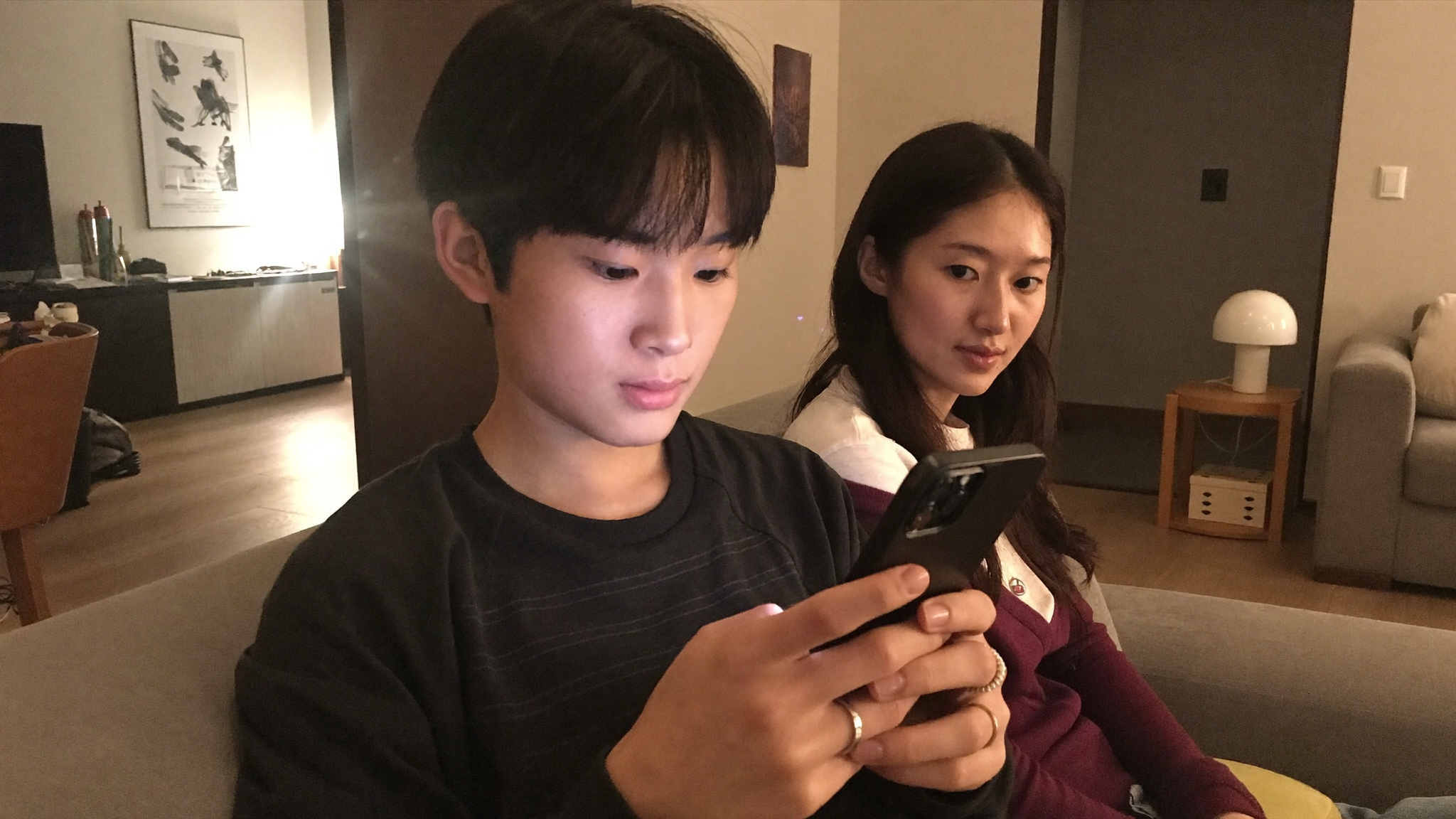 韩国青少年在家看手机,家长在旁边关注,象征社交媒体禁令争议的图片