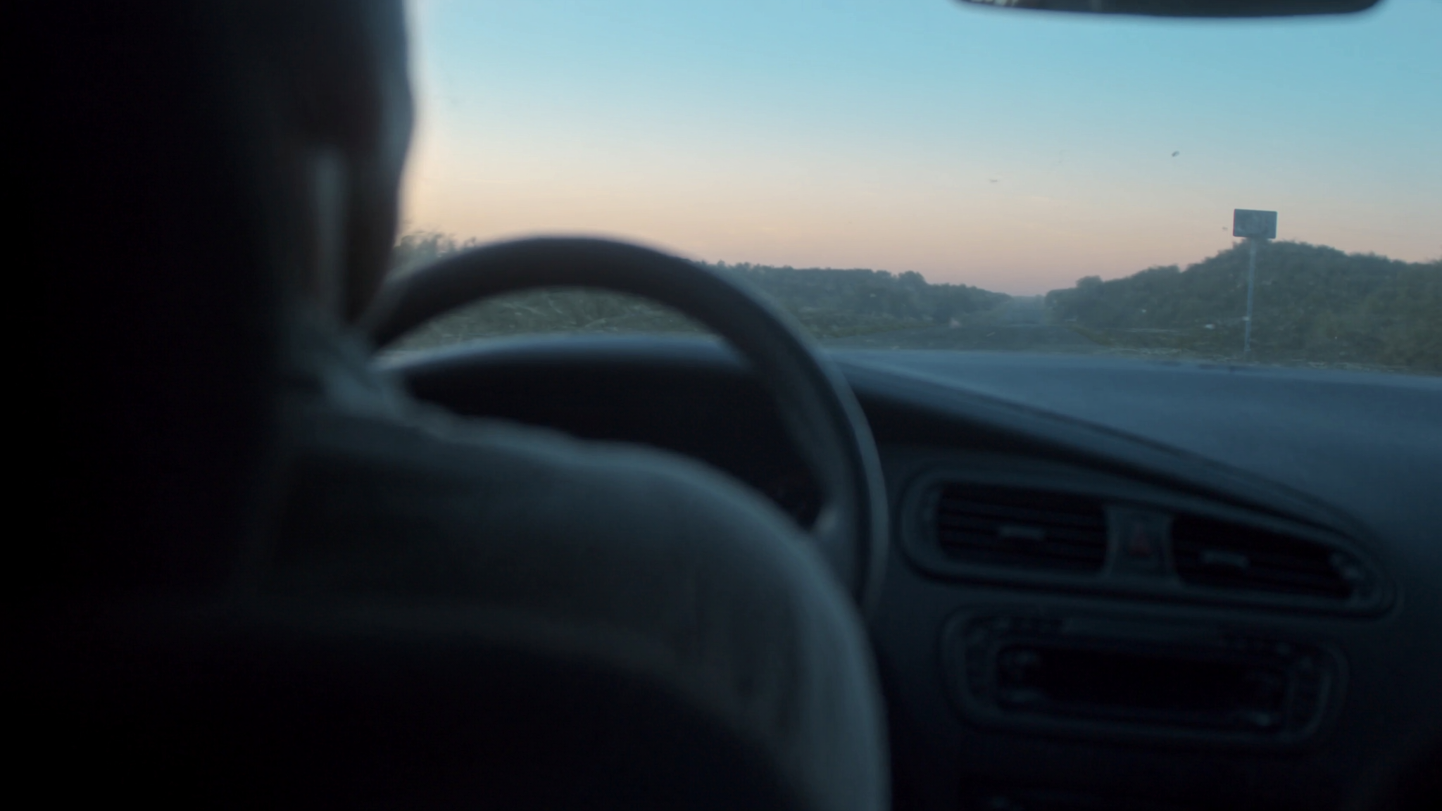 Vue depuis l interieur d une voiture a l aube, volant au premier plan et route de campagne deserte
