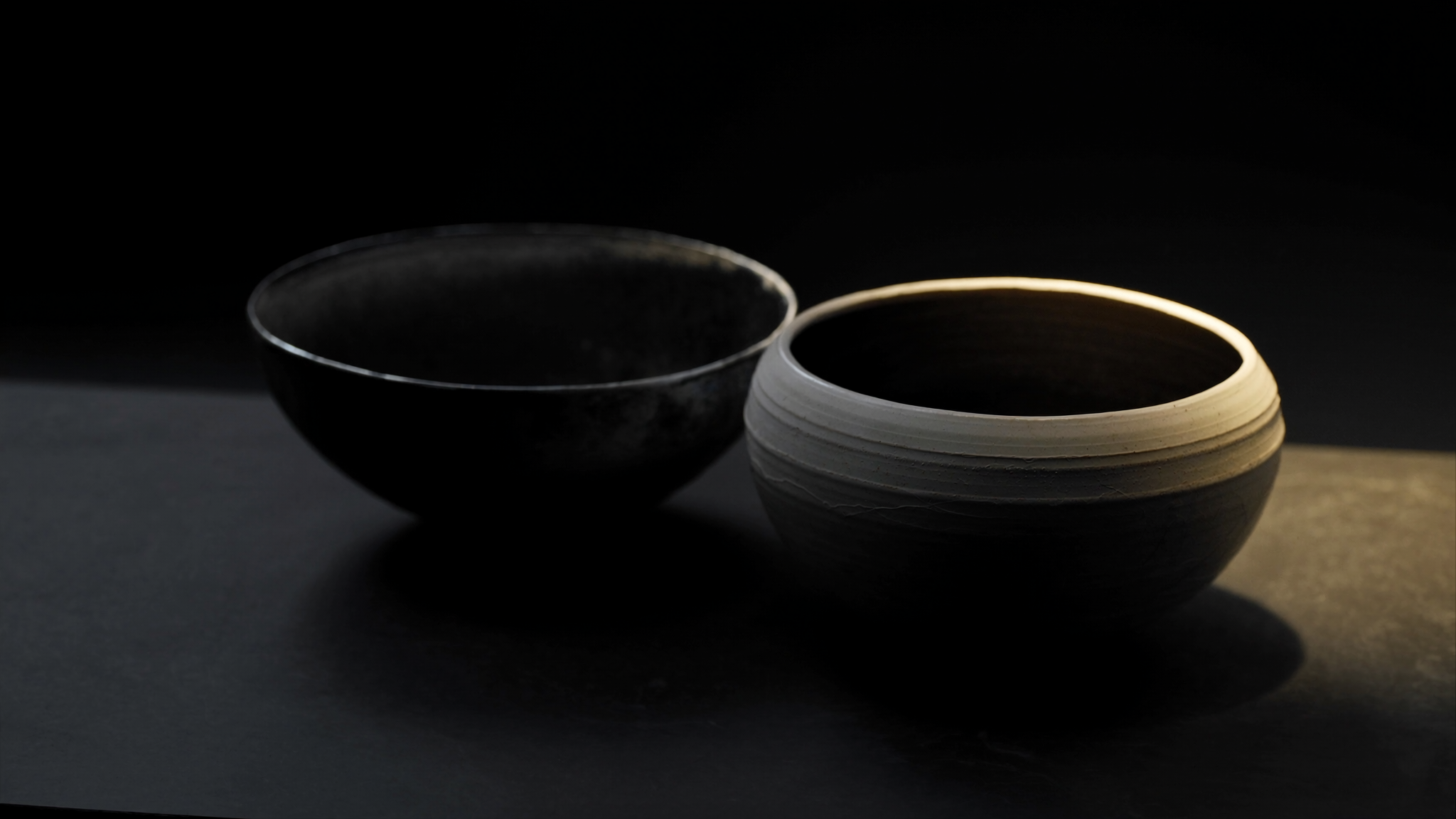 Deux bols en ceramique artisanale vides, un clair et un anthracite, poses sur une ardoise sombre