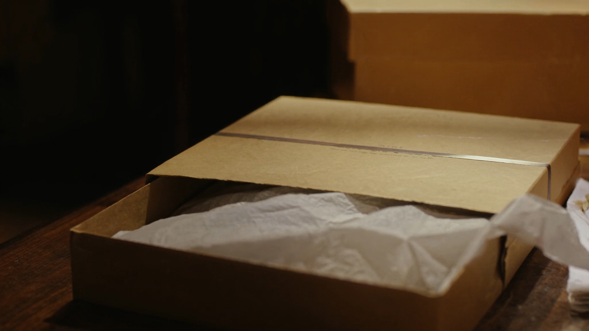 Boite cadeau en kraft ouverte et vide avec papier de soie froisse et ruban fin sur table en bois