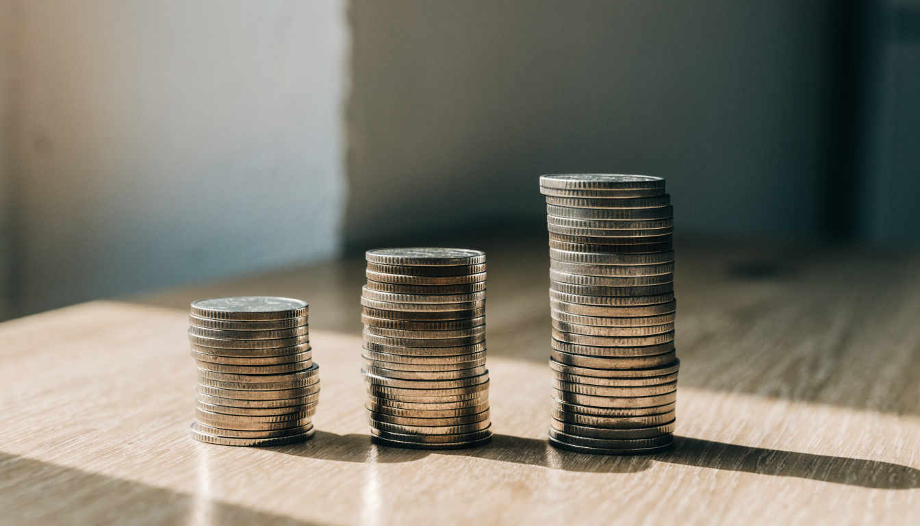 Trois piles de pièces de monnaie de hauteurs croissantes alignées sur un bureau en bois clair