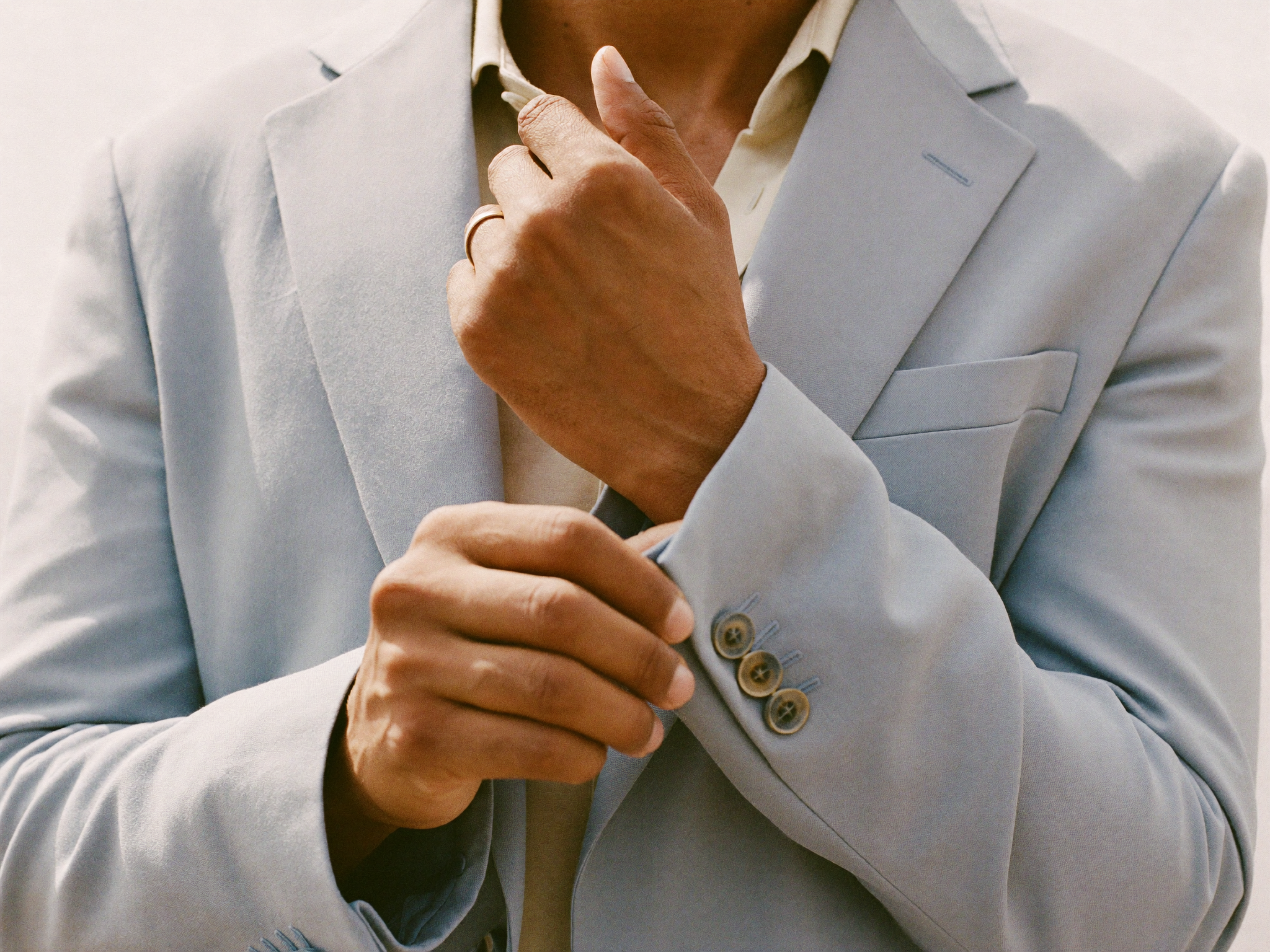 Close view of a man adjusting the cuff of a soft powder-blue summer suit in bright daylight