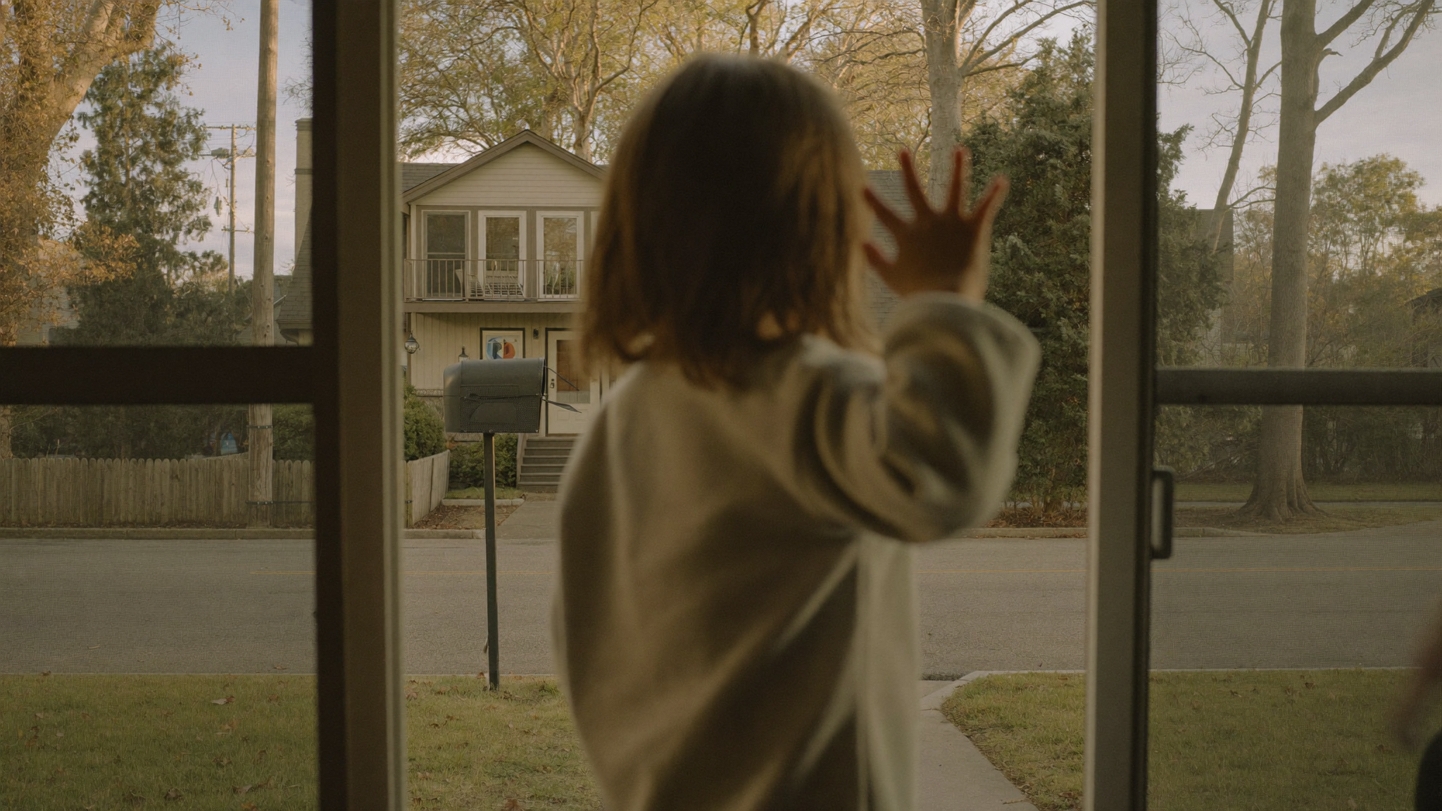Child at the front door, hand raised in a wave toward the street in golden morning light