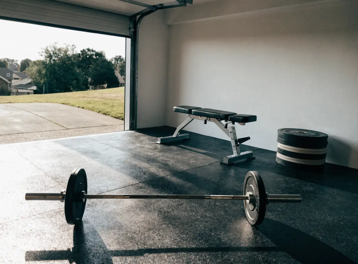 Clean minimal home garage gym with barbell, plates, and bench