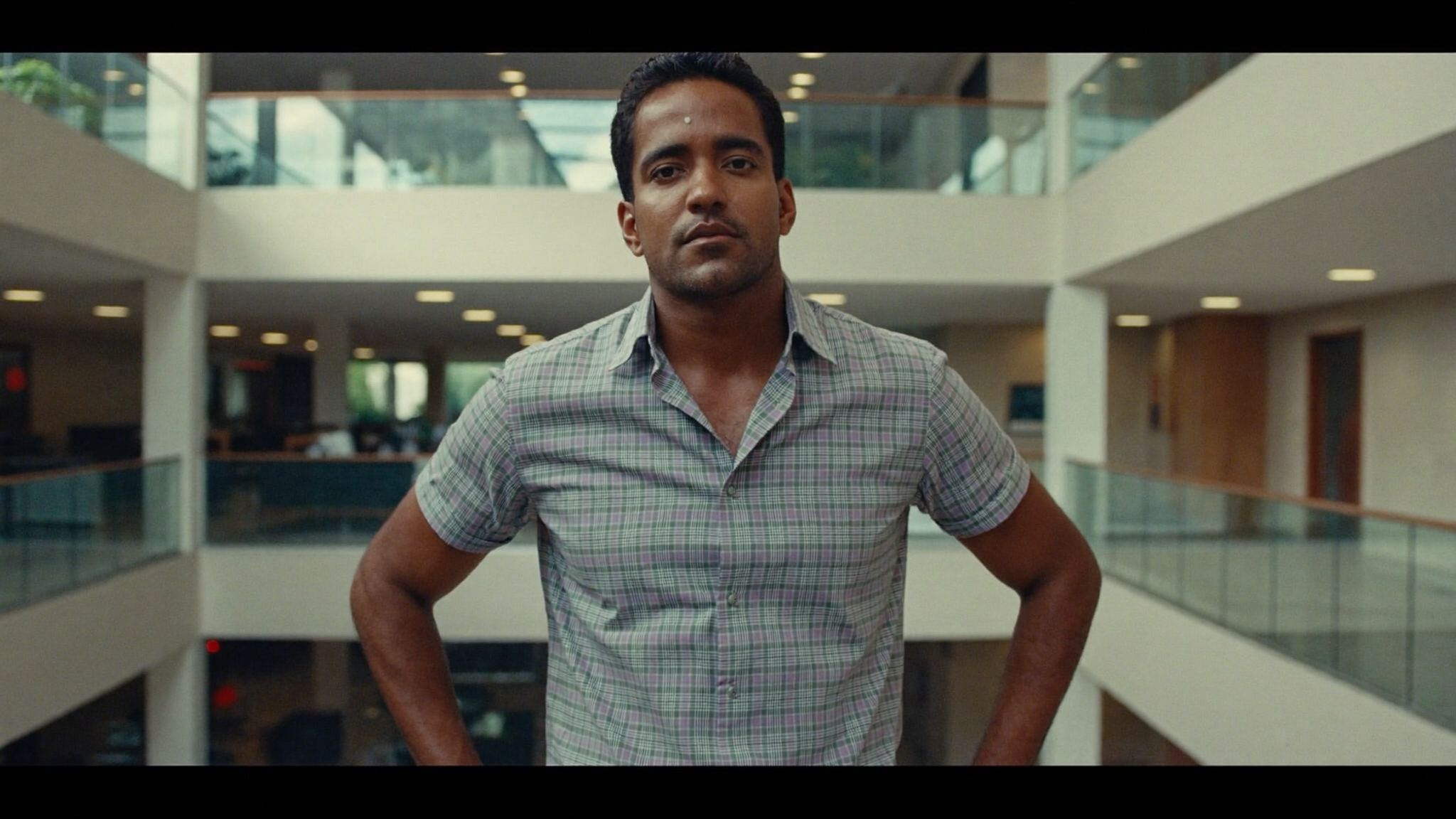 South Asian man in his 30s standing confidently in a modern office atrium, smart casual, arms relaxed, natural daylight