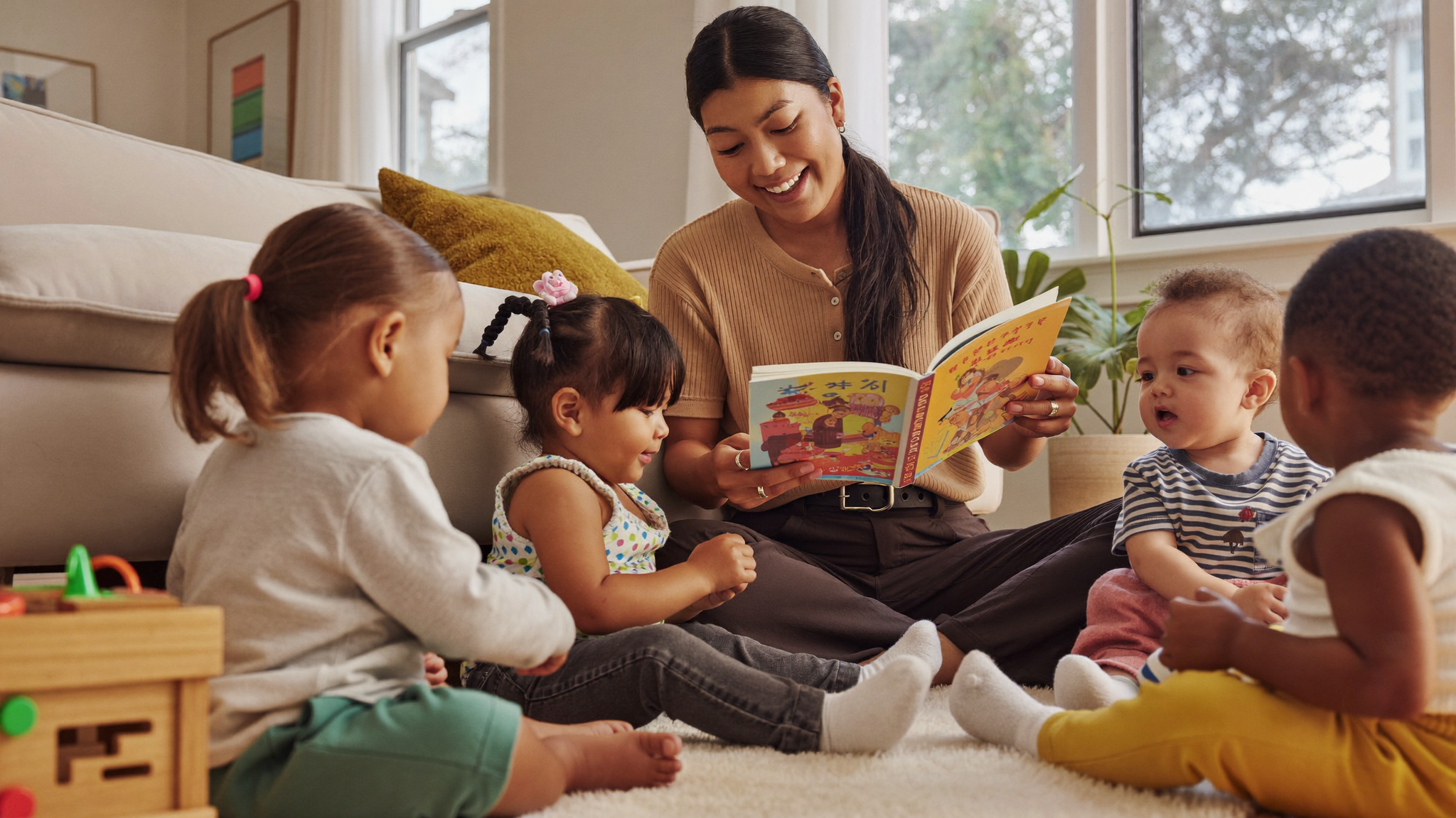 Caregiver reading a picture book to toddlers in a bright home daycare