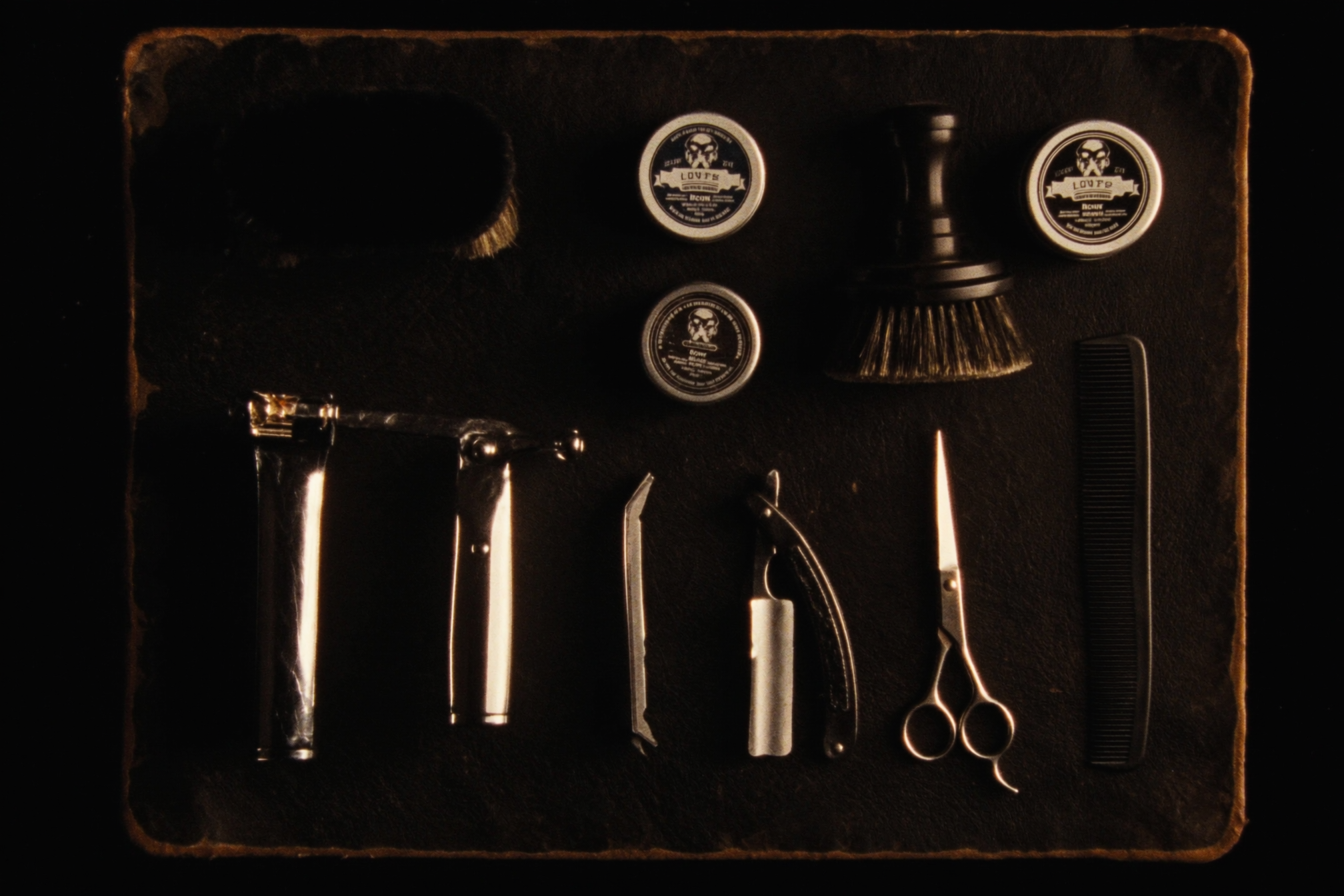 Flat lay of barber tools — clippers, straight razor, scissors, comb and pomade on leather