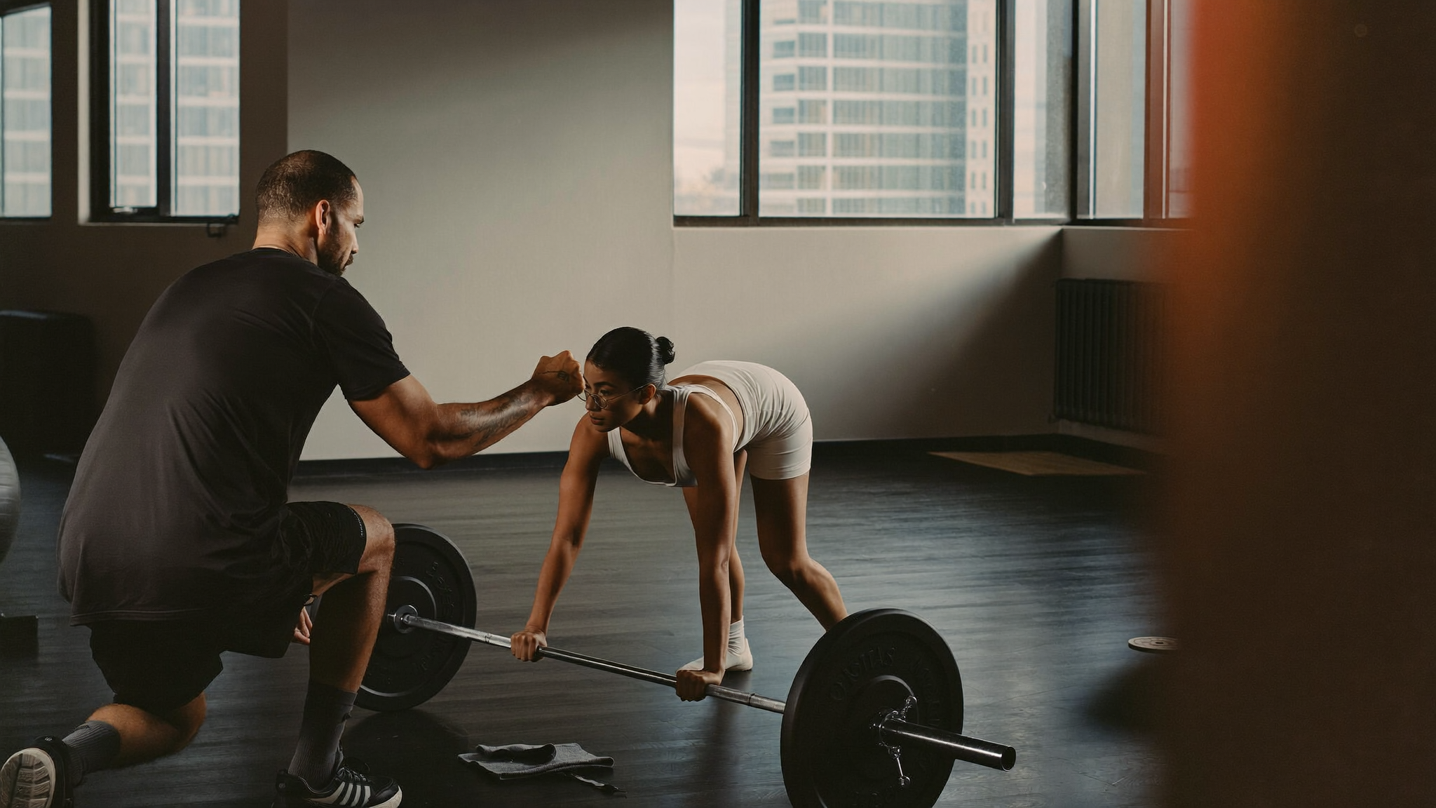 Personal trainer spotting a client on a barbell in a modern gym