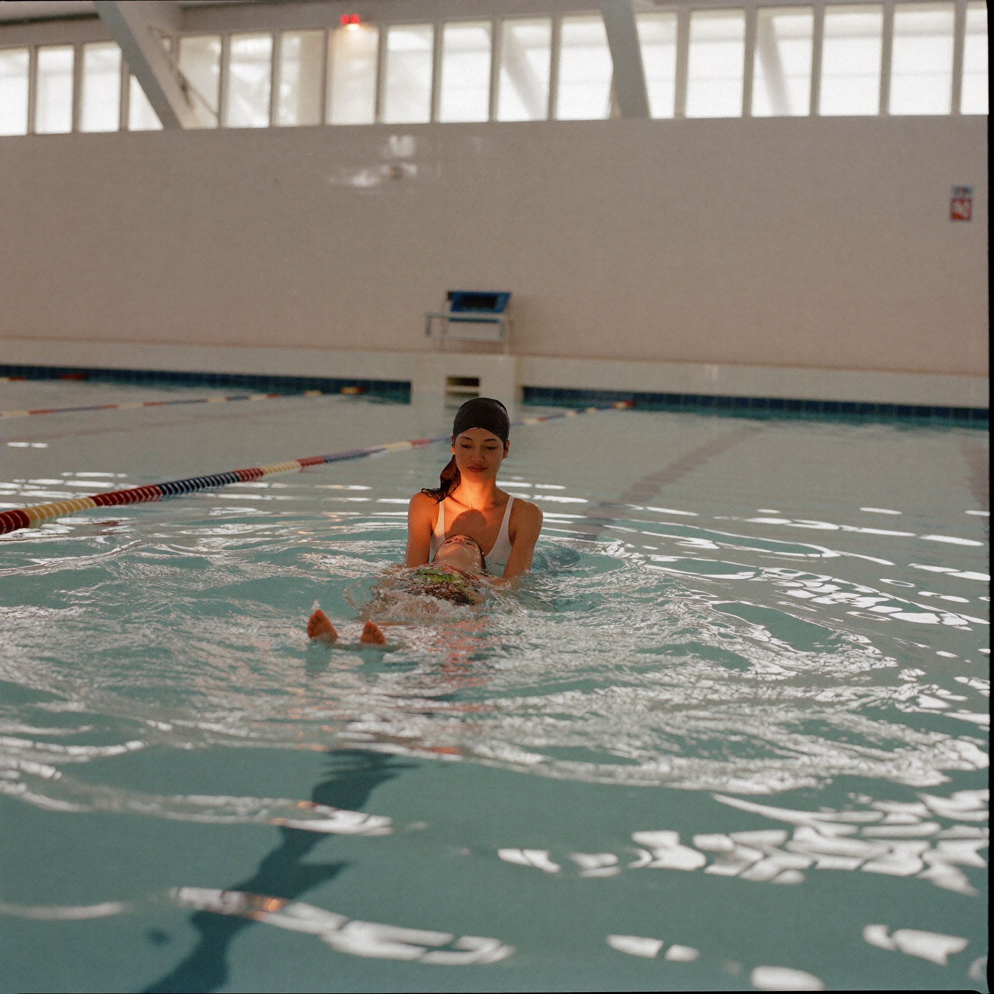 Swim instructor supporting a young child floating in a bright indoor pool