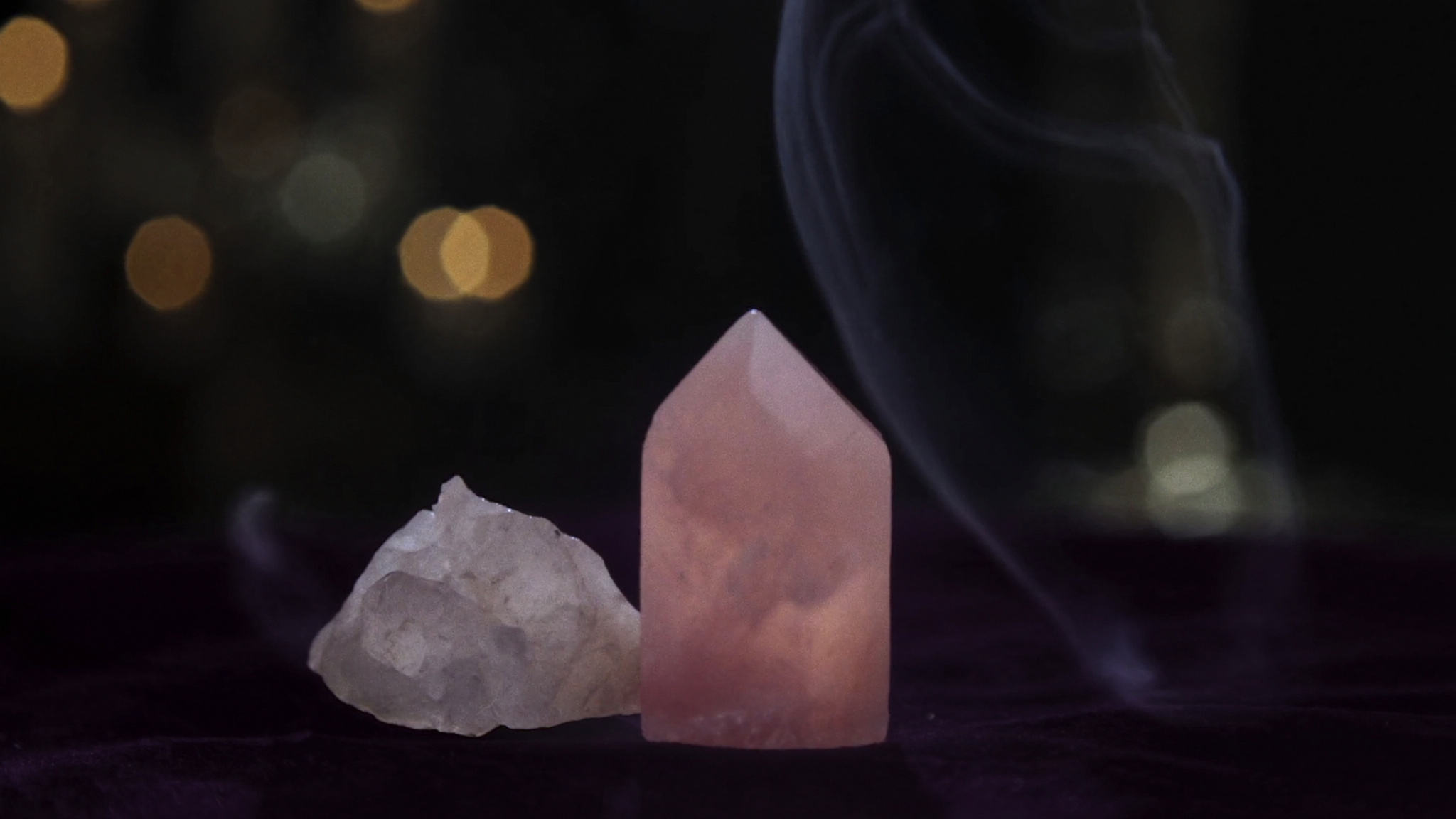 A rose quartz point and clear quartz cluster in candlelight with incense smoke