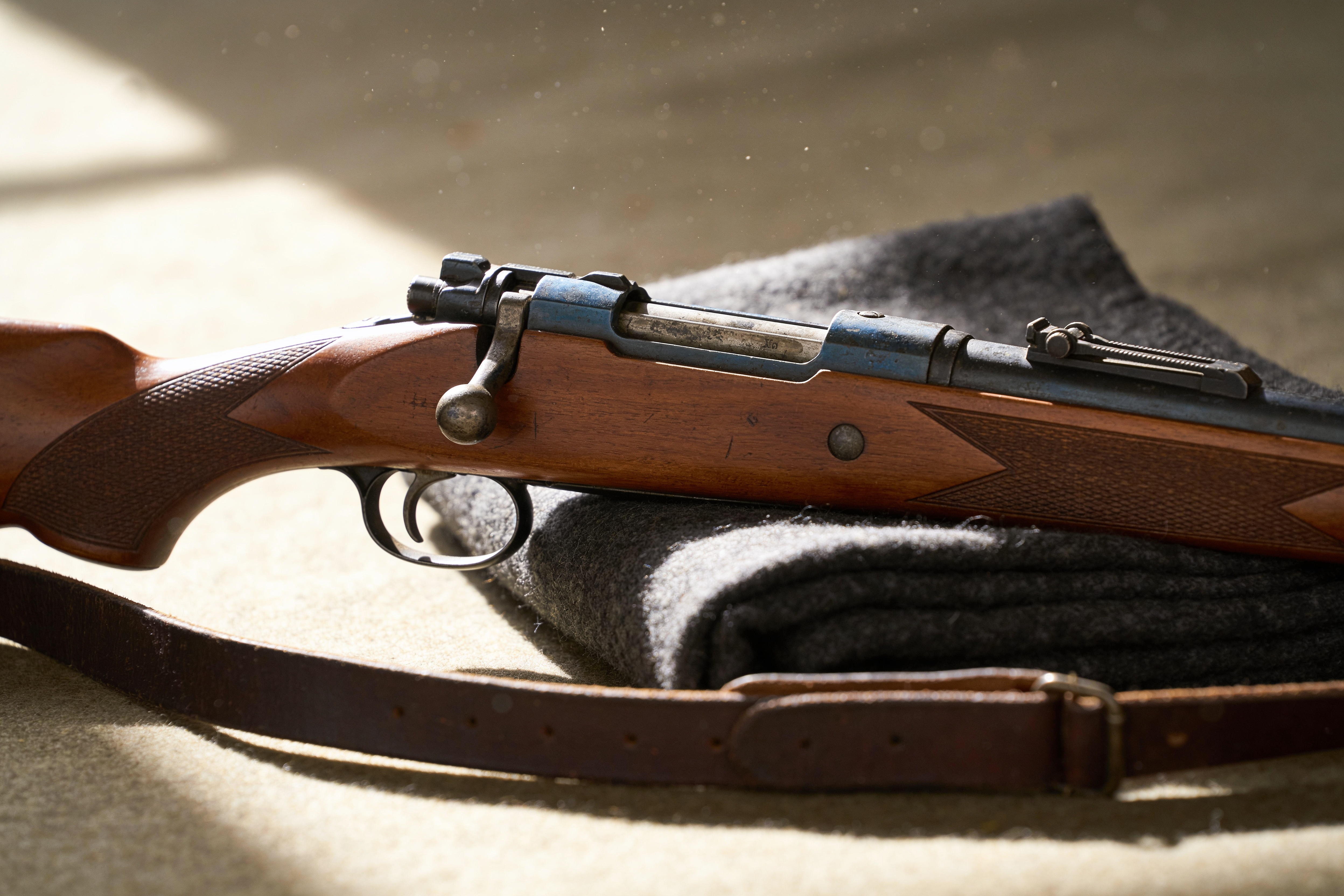 An old walnut-stocked bolt action rifle resting on a folded wool blanket in soft window light
