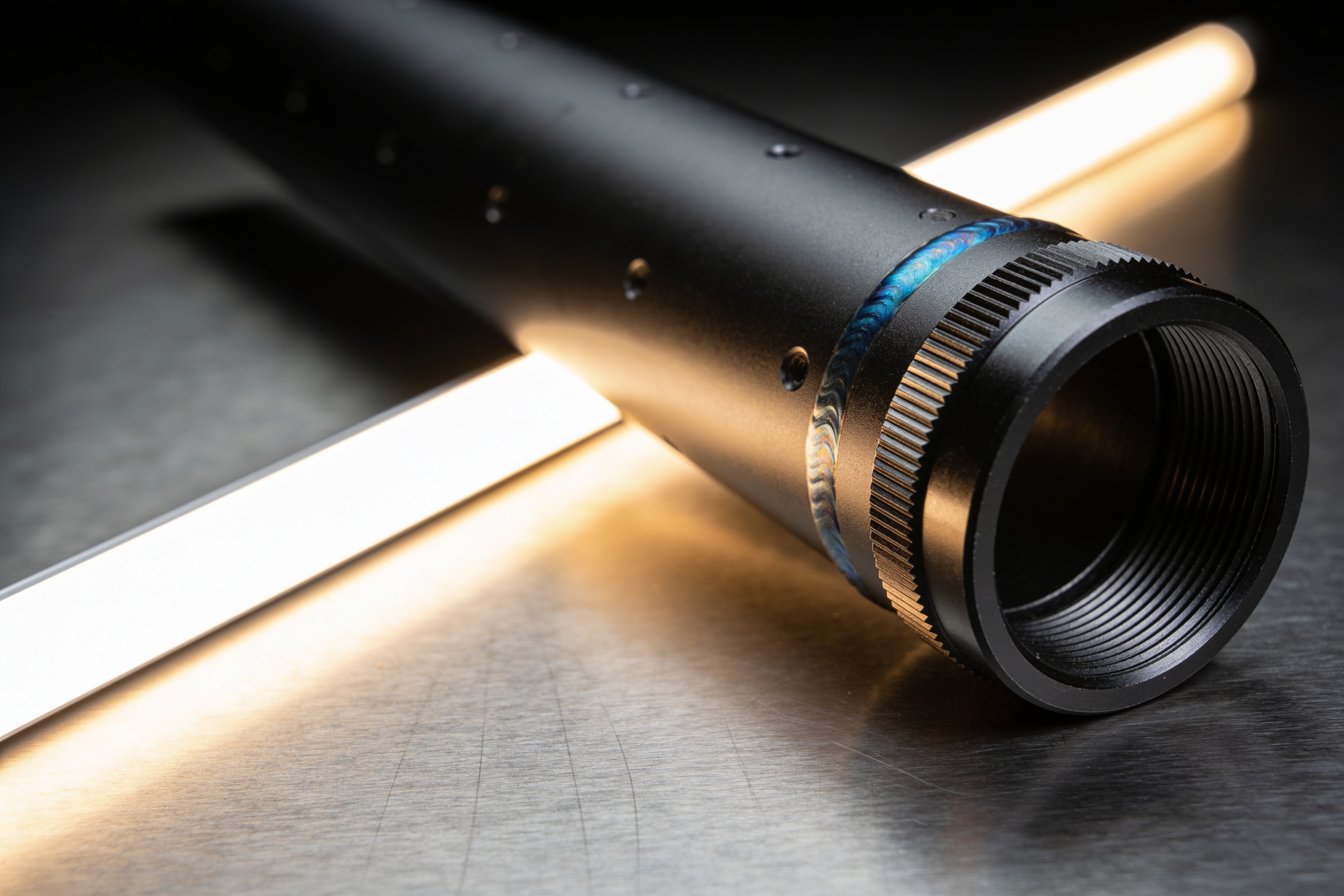 A matte black machined cylindrical firearm component lit from behind on a dark surface