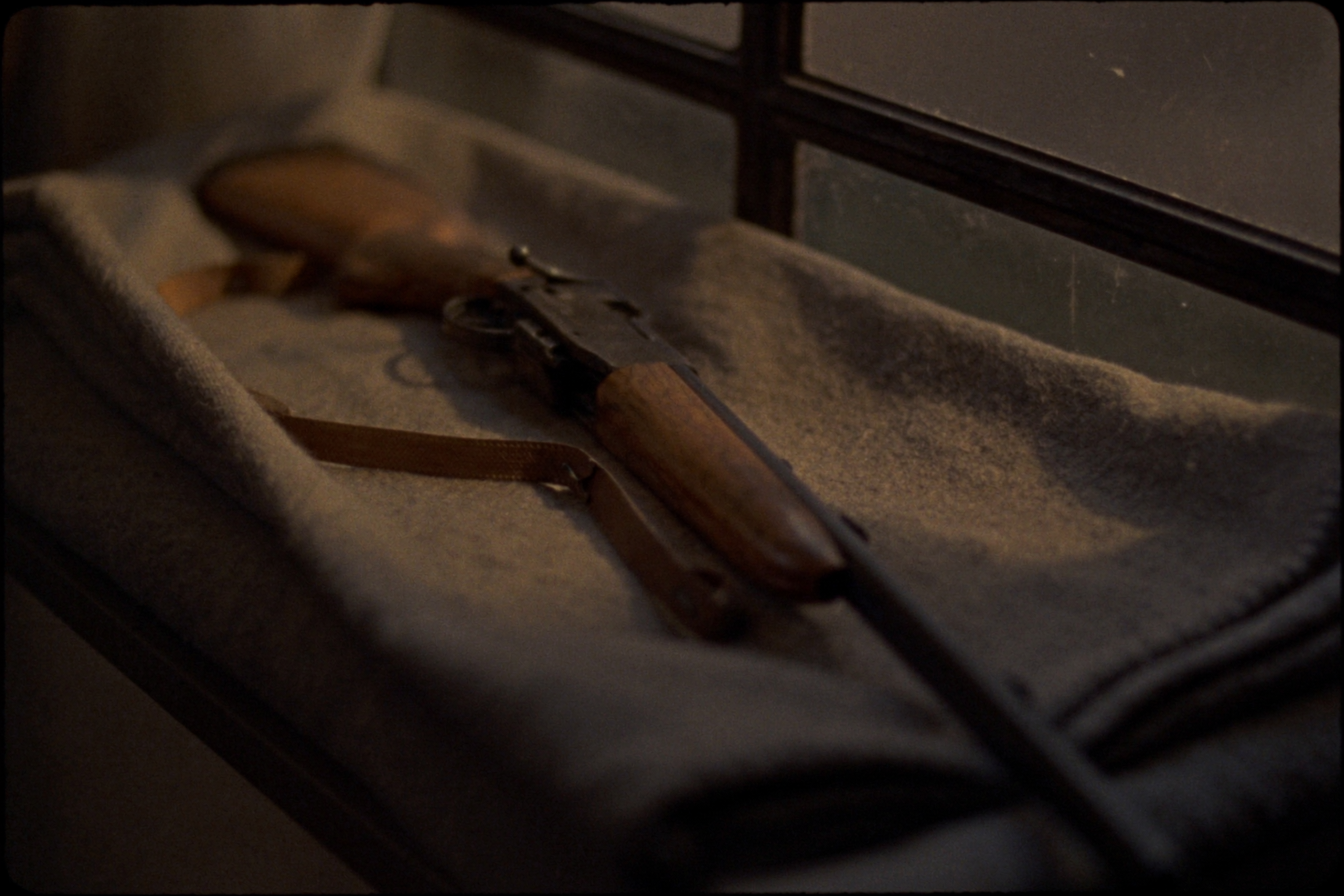 An old walnut-stocked bolt action rifle on a folded wool blanket in soft window light