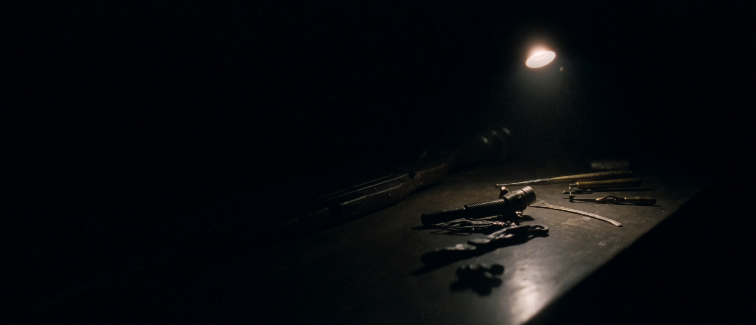 A gunsmith's workbench under a single task lamp, precision tools receding into darkness