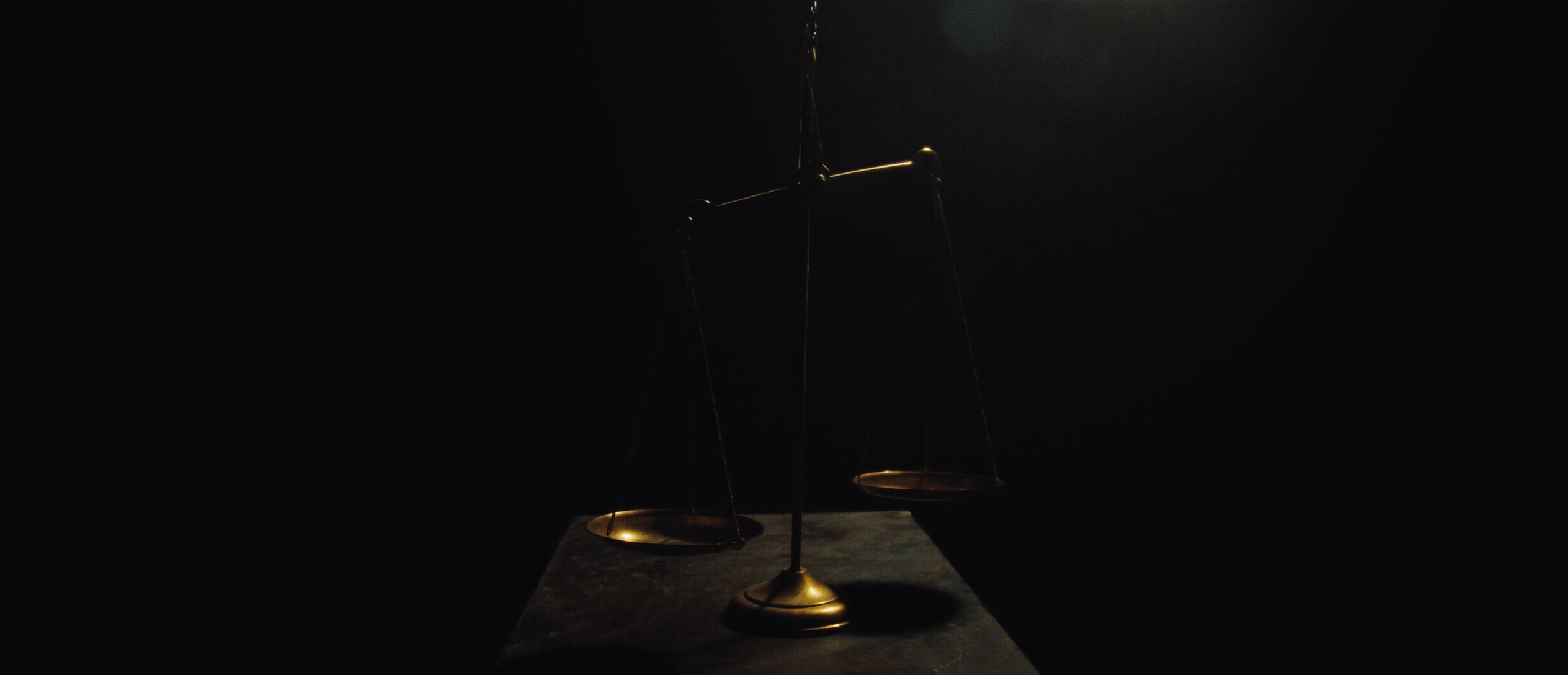 An antique brass balance scale rim-lit against darkness