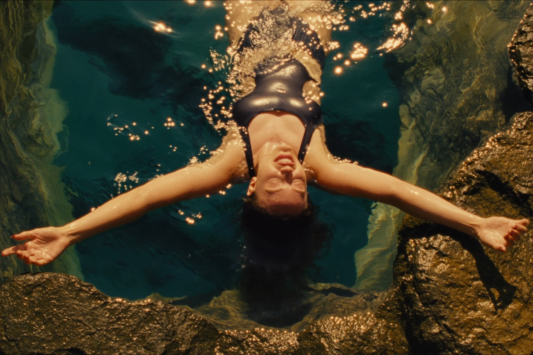 A swimmer floating in a sunlit natural rock pool
