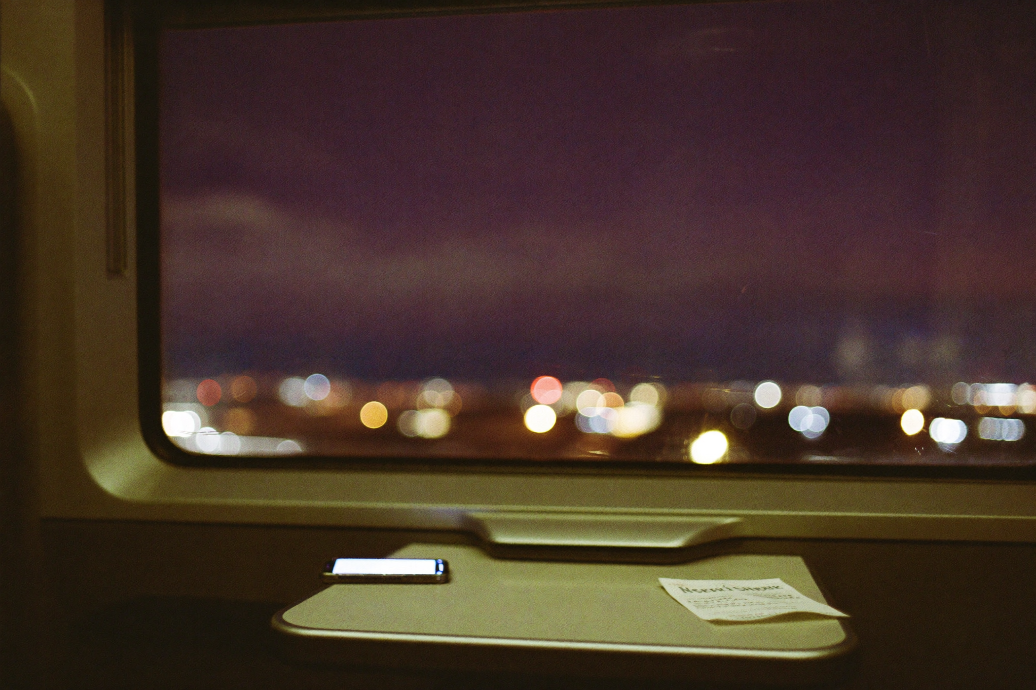 Night train crossing Europe - city lights past the window, a phone glowing on the fold-down table