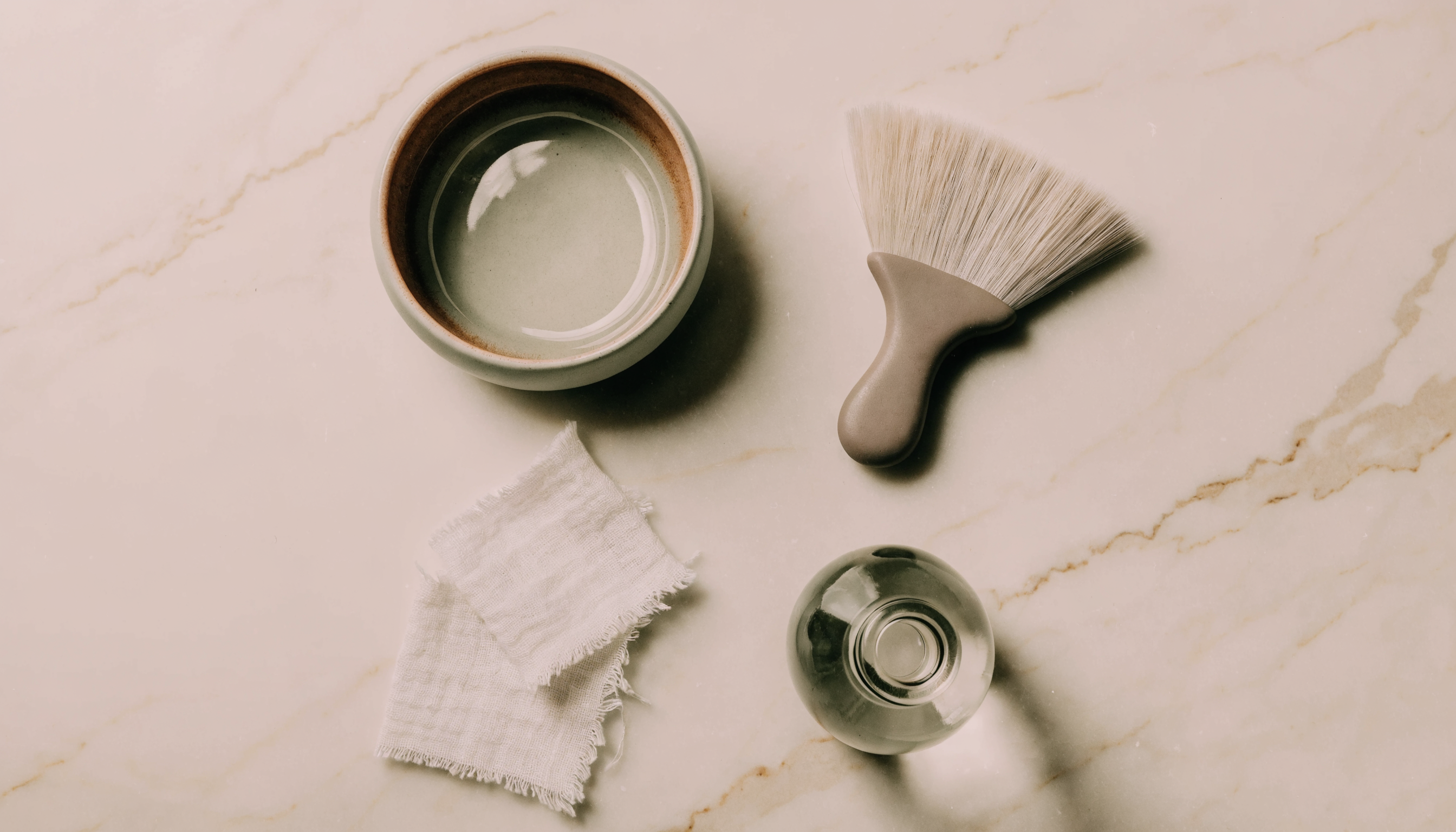 A marble flat lay with a treatment bowl and a fan brush