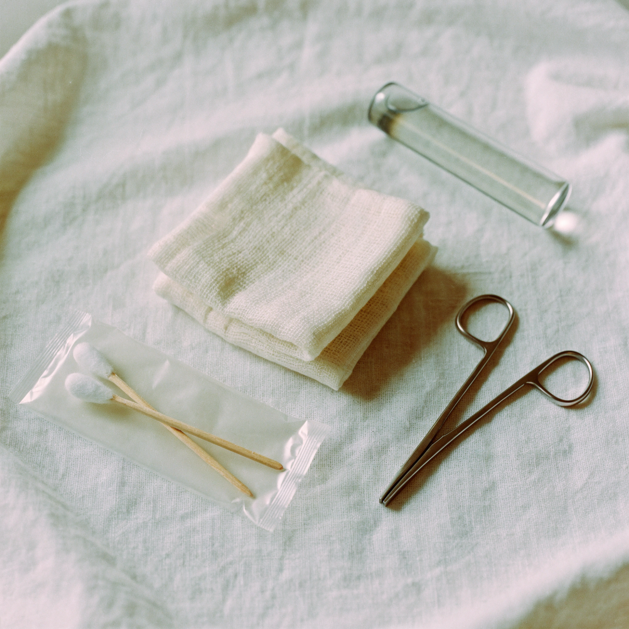 Gauze, a swab, forceps and a small vial laid out on a tray
