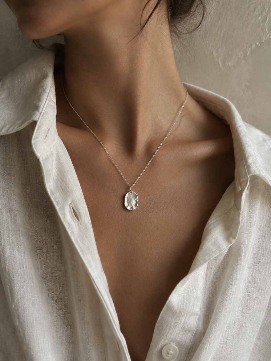 A small irregular silver pendant on a fine chain at the collarbone