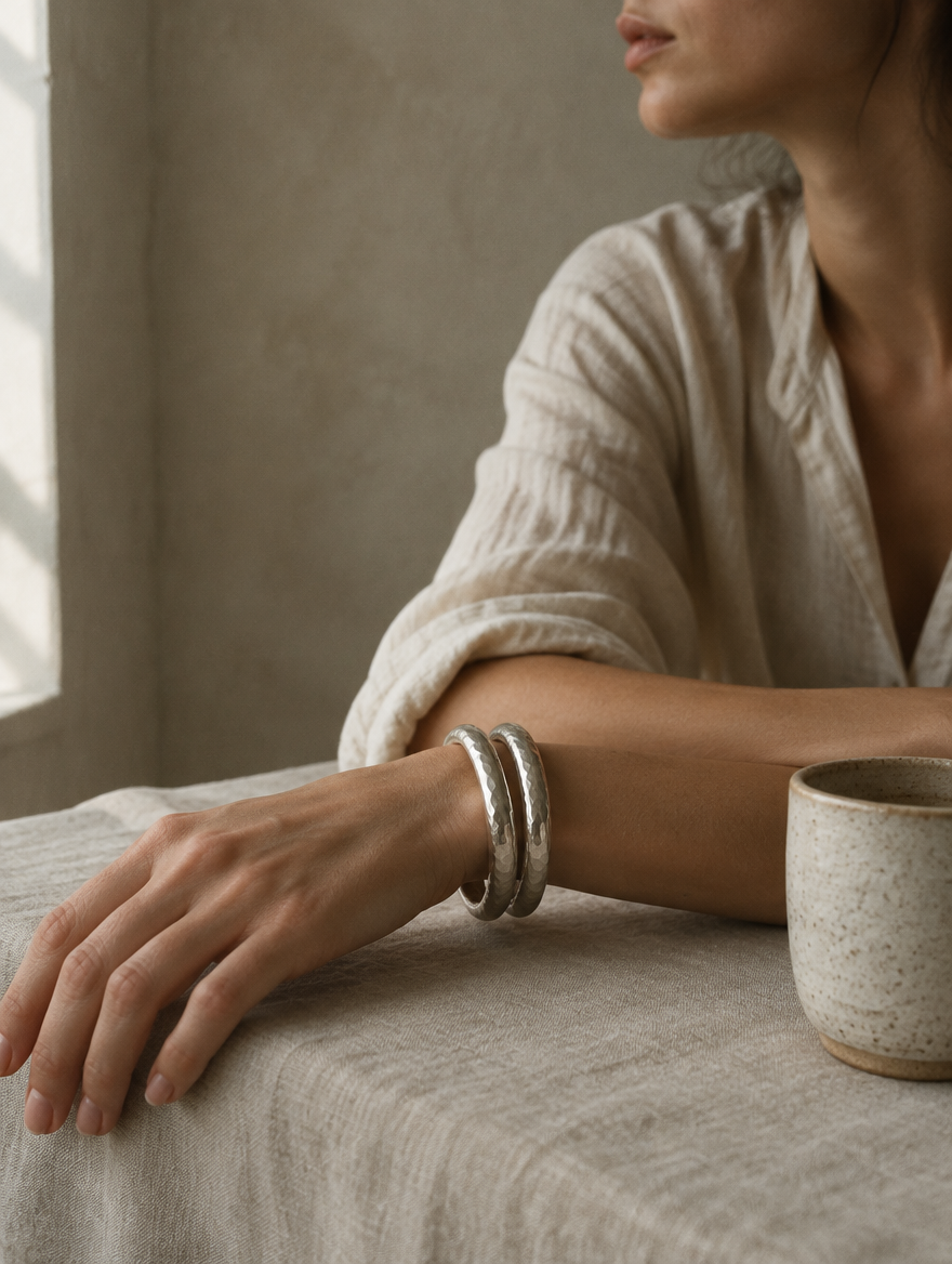 Two hammered silver bangles on a wrist resting on linen