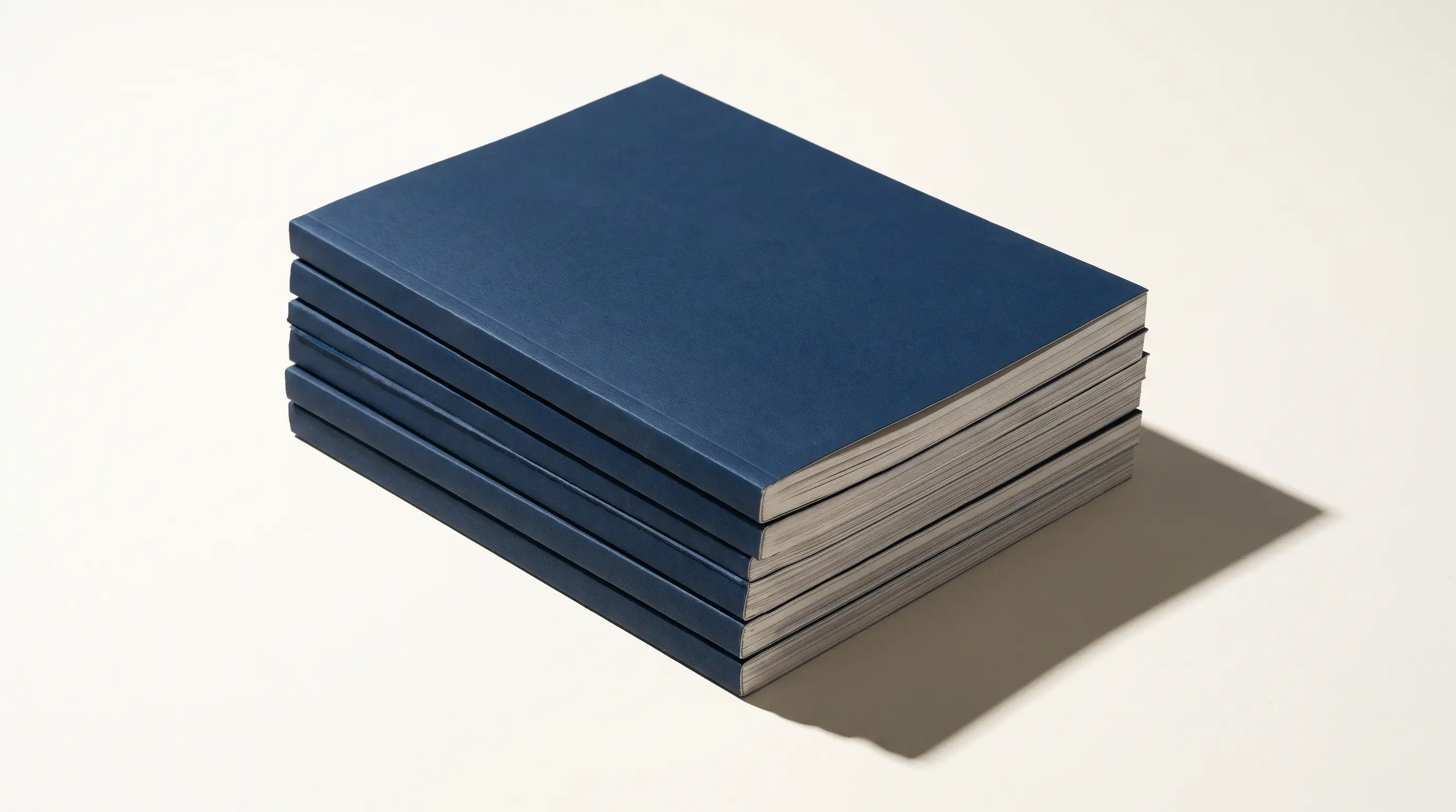Stack of navy editorial journals on a warm white surface