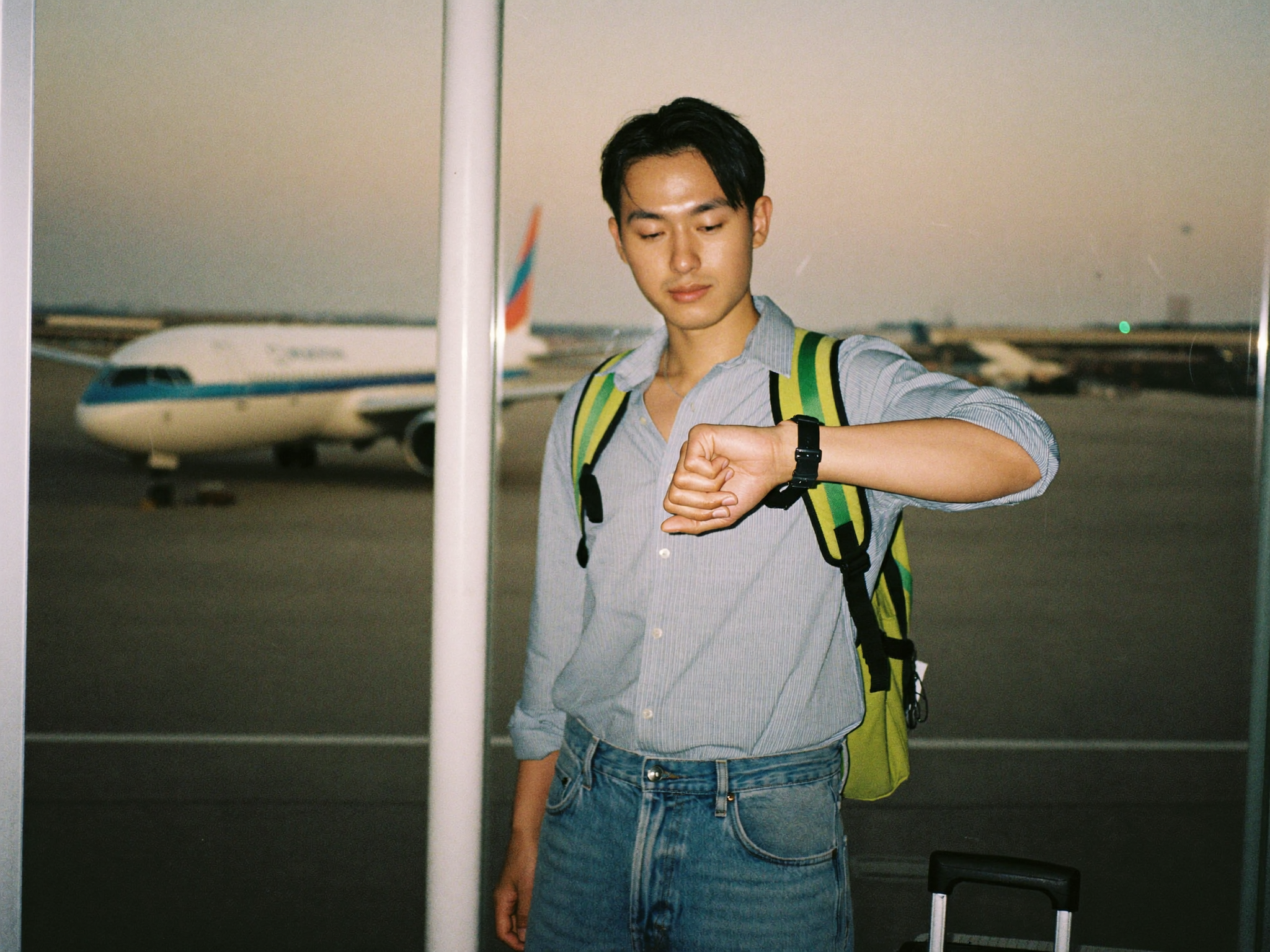 공항 창가에서 손목시계를 보며 초조하게 기다리는 여행객과 유리창 밖의 비행기