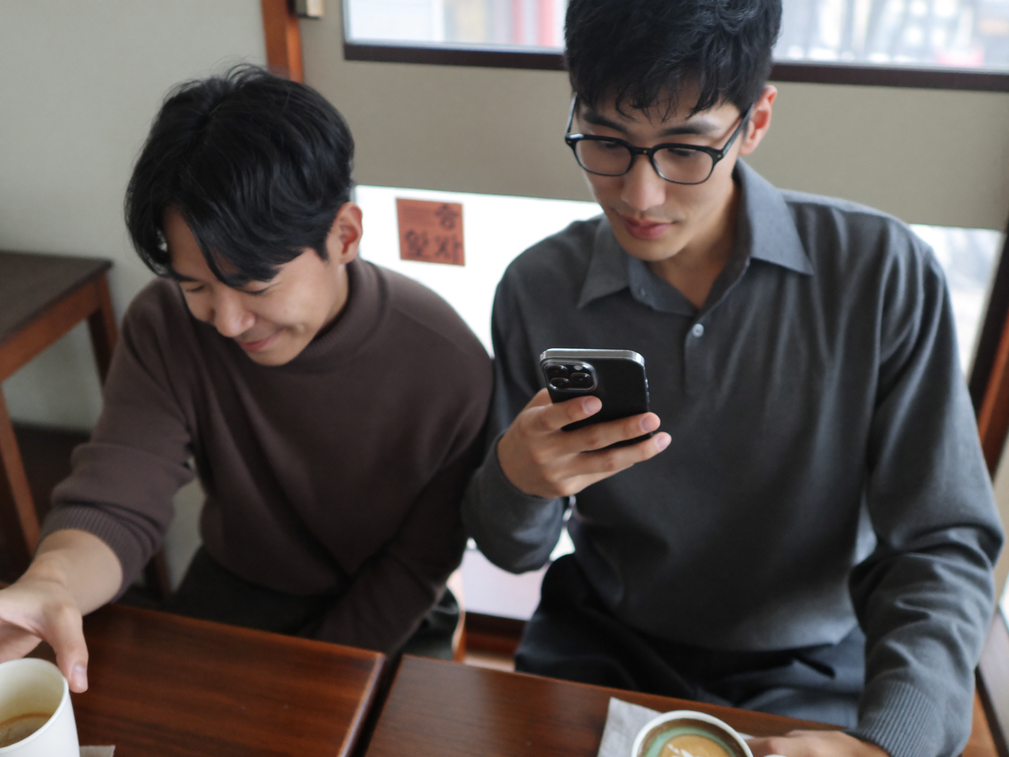 카페에서 마주 앉아 어색한 분위기 속에 대화하는 두 남성, 친구 사이의 돈 문제를 상징하는 이미지