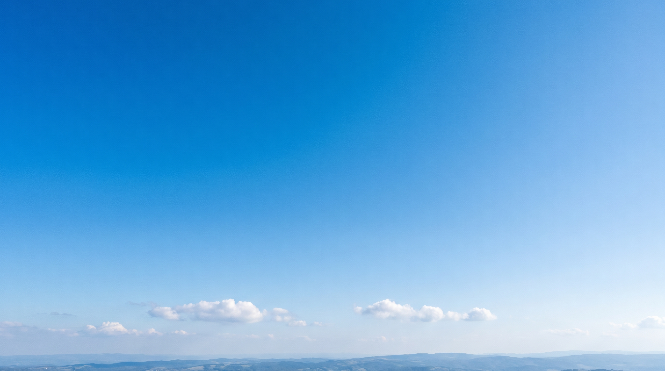 A clear deep blue daytime sky with a few white clouds over a horizon