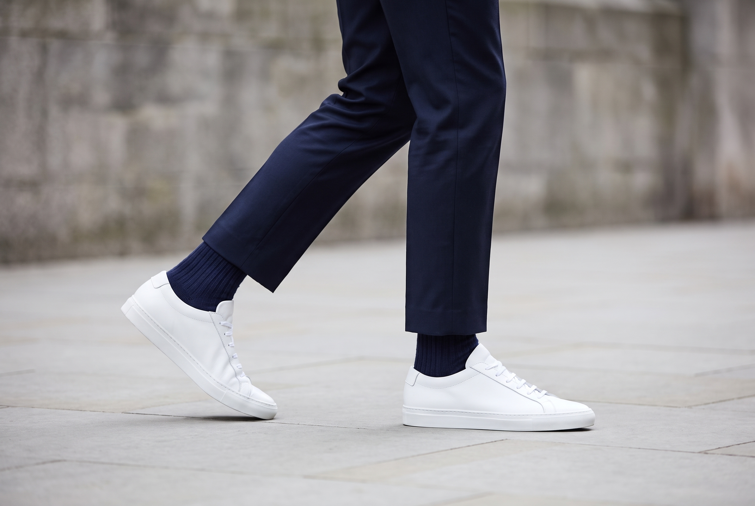 Ribbed navy Sockateur socks worn with a white smart sneaker and tailored navy trousers on a city street