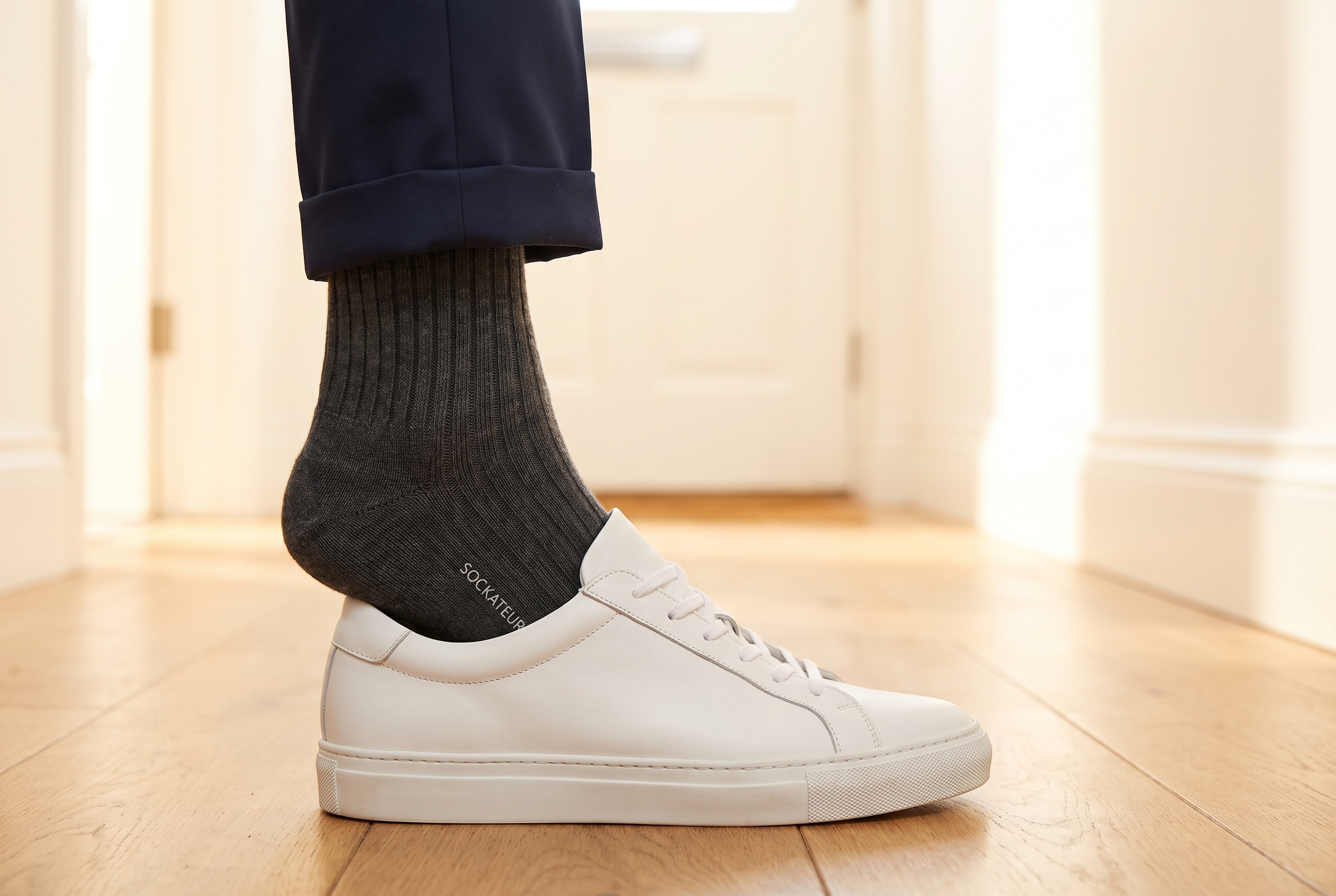 Close-up of a foot in a Sockateur Classic black sock stepping into a white smart sneaker