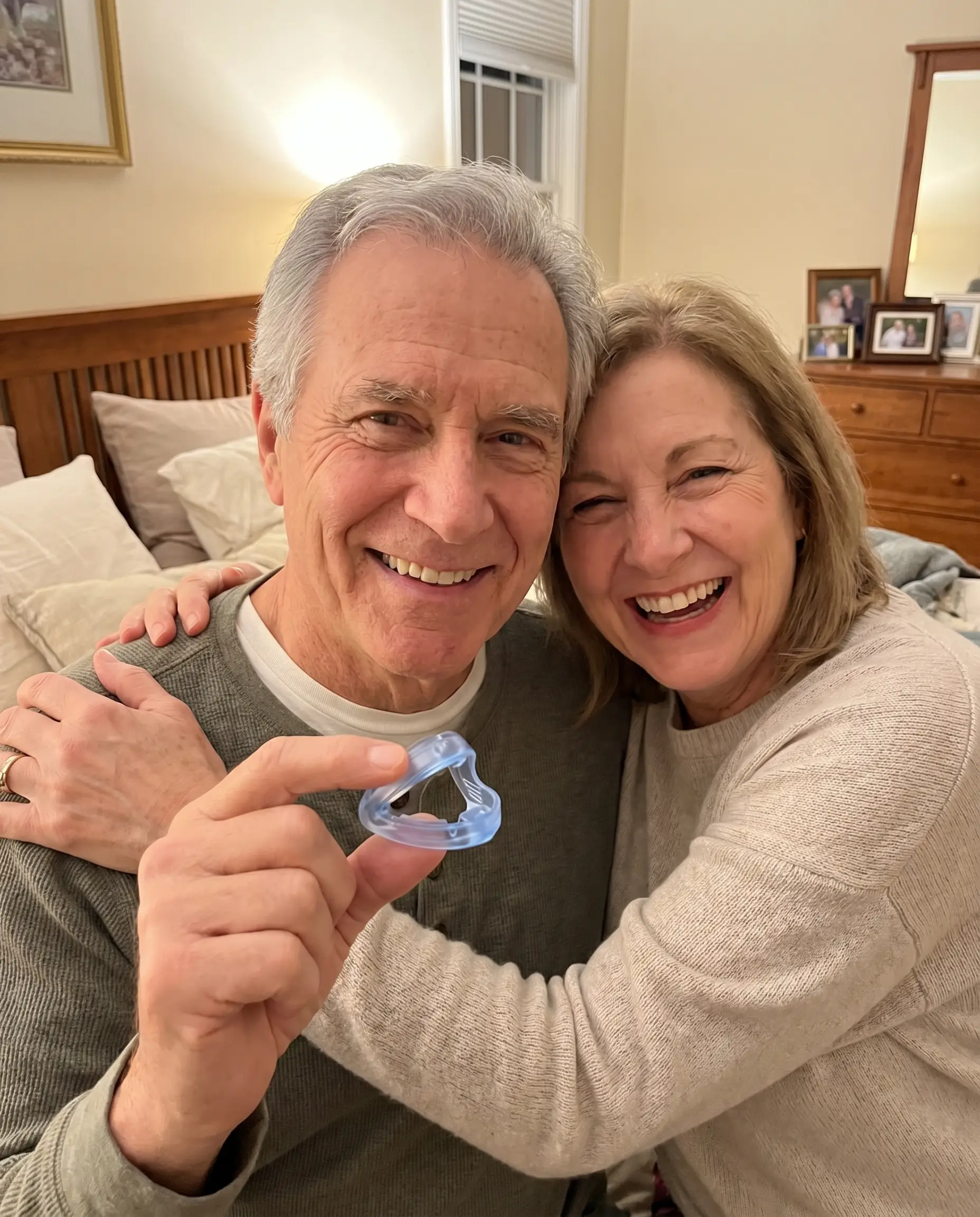 An older couple smiling and holding the clear QuietNight mouthpiece