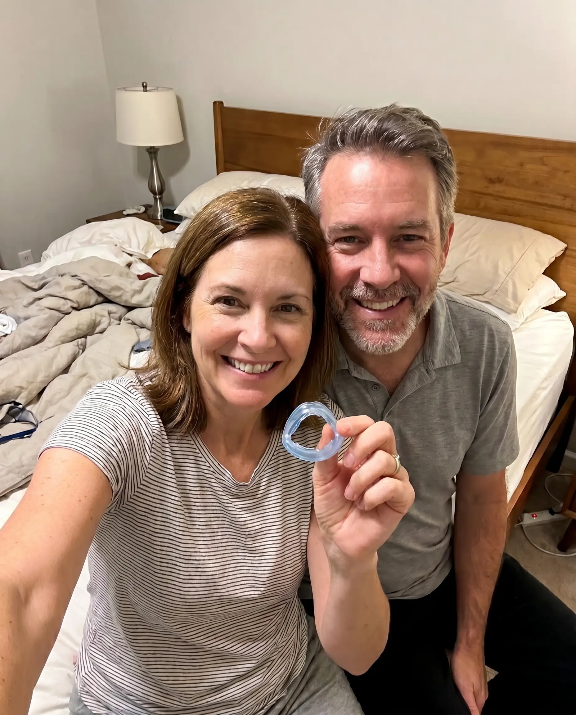 A happy middle-aged couple holding the clear QuietNight mouthpiece in their bedroom
