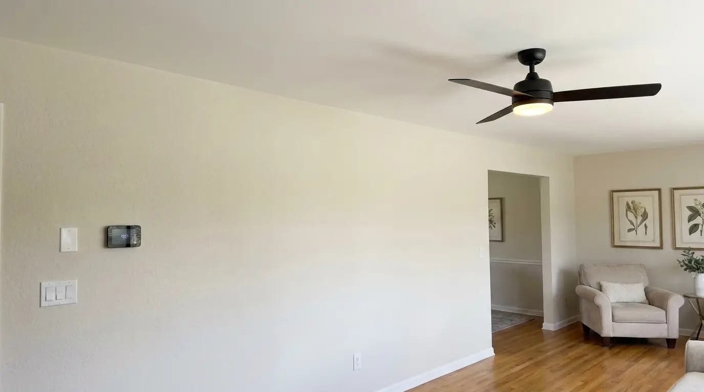 Same room after: new matte black ceiling fan glowing, new outlet, rocker switch and smart thermostat installed