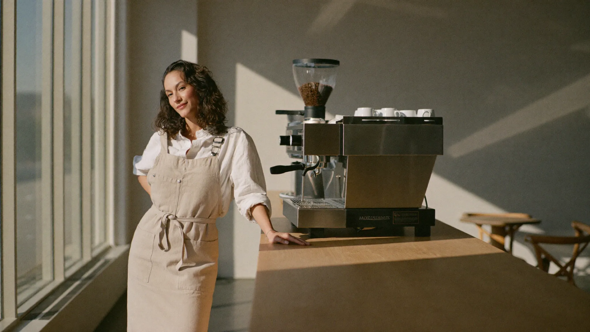 Owner of a specialty coffee roastery standing beside the espresso machine in her cafe in morning light