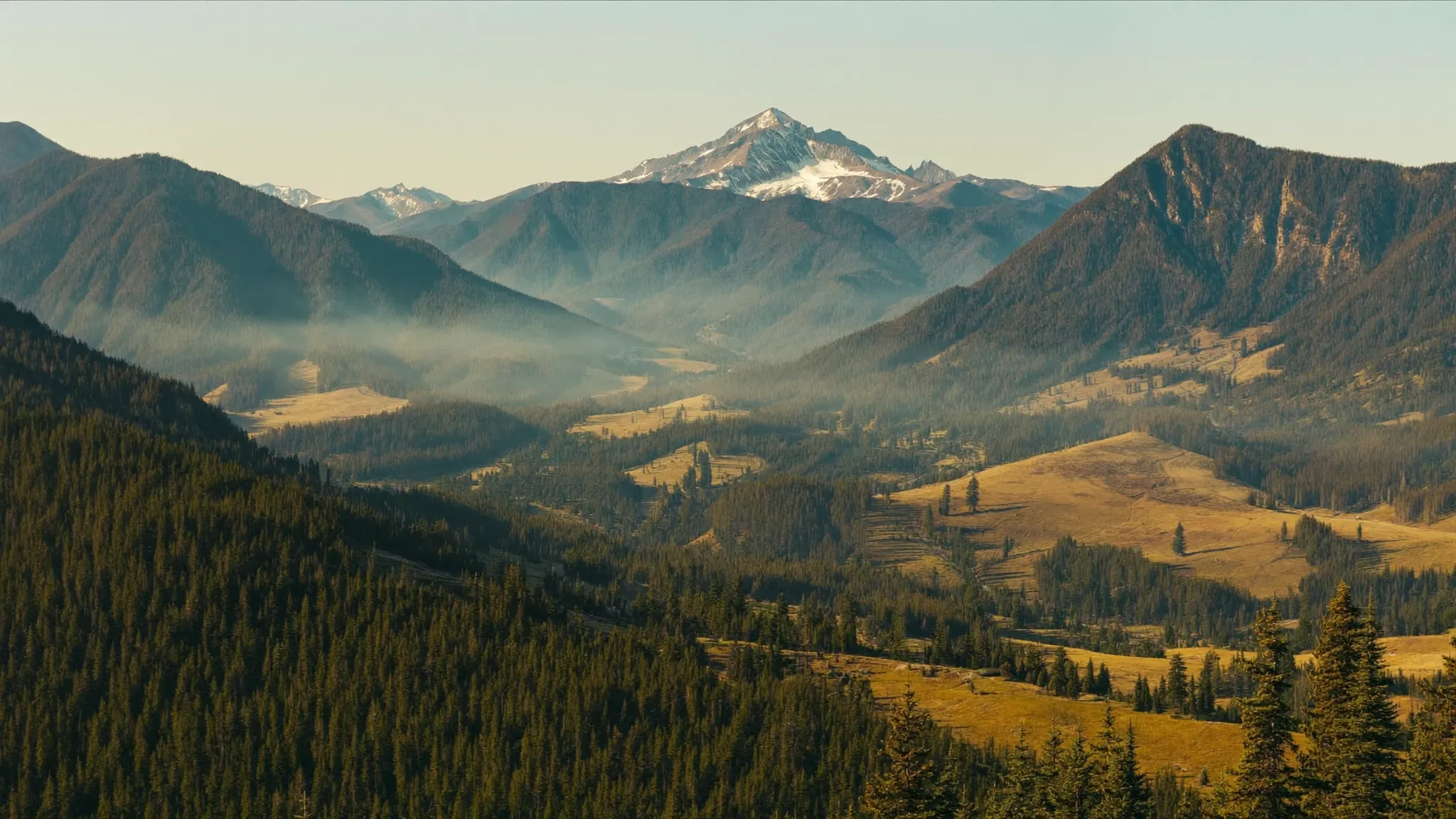 A high Rocky Mountain basin in early September with dark timber, golden grass parks and smoke haze from distant wildfire