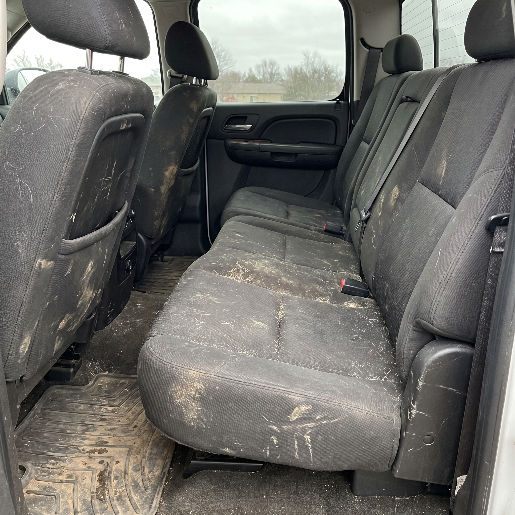 Pickup truck crew cab back seat with dark upholstery covered in dog hair, dried mud and scuffs, no cover