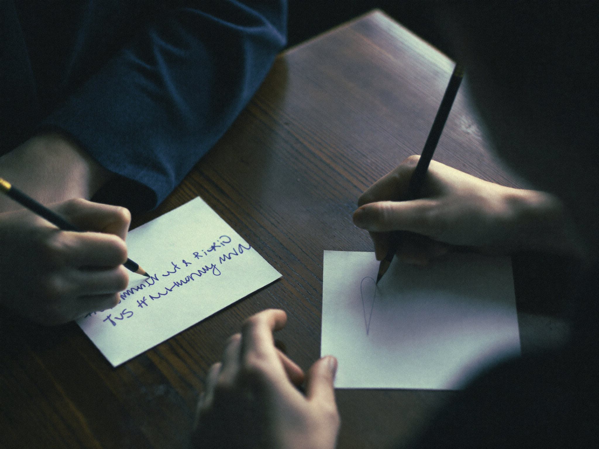 Close crop of hands writing independently on blank cards at a shared table
