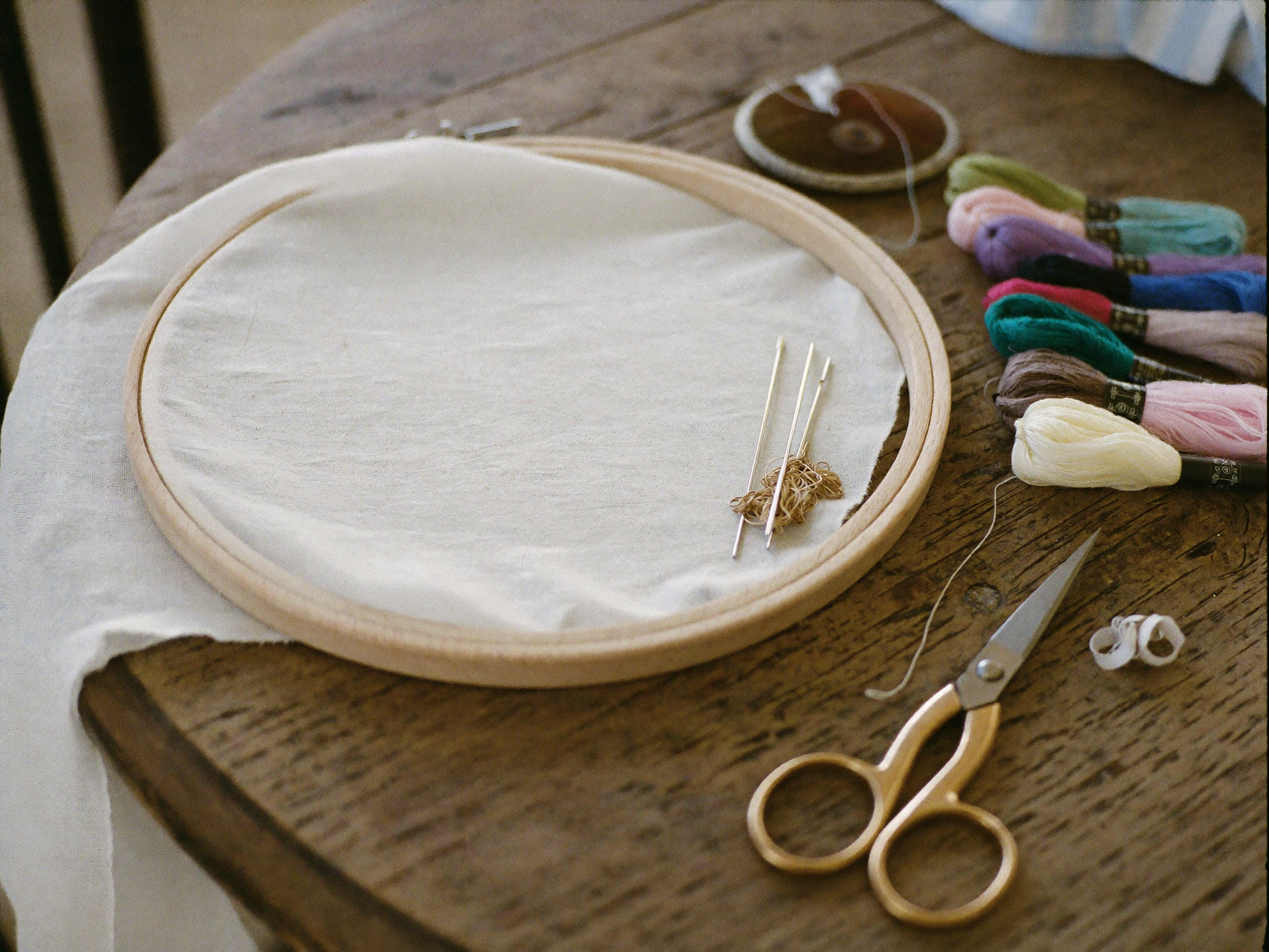 Matériel de broderie disposé sur une table : tambour, fils, aiguilles et ciseaux