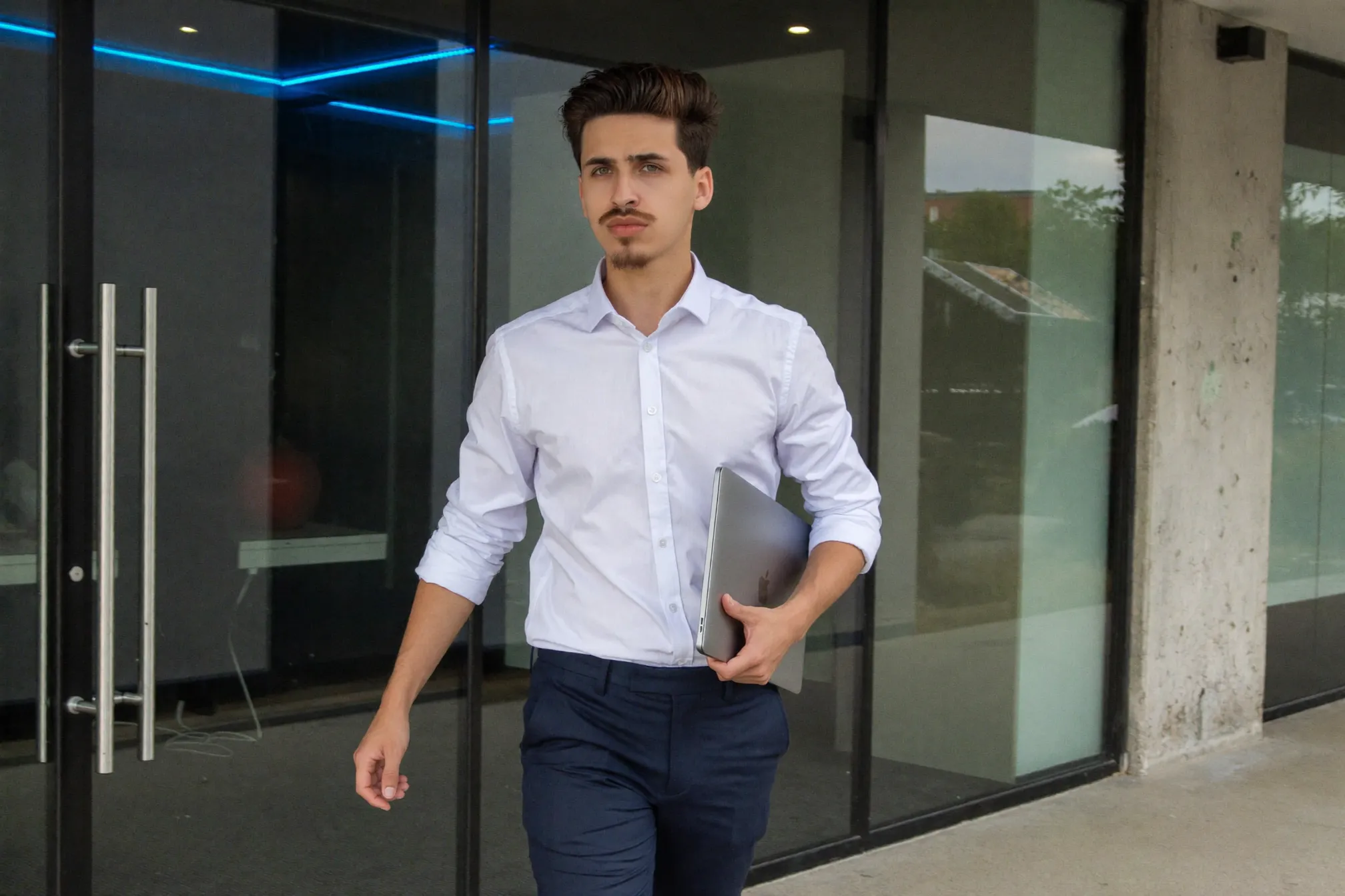 Daniel walking through the Progon office with a laptop, blue accent lighting along the wall