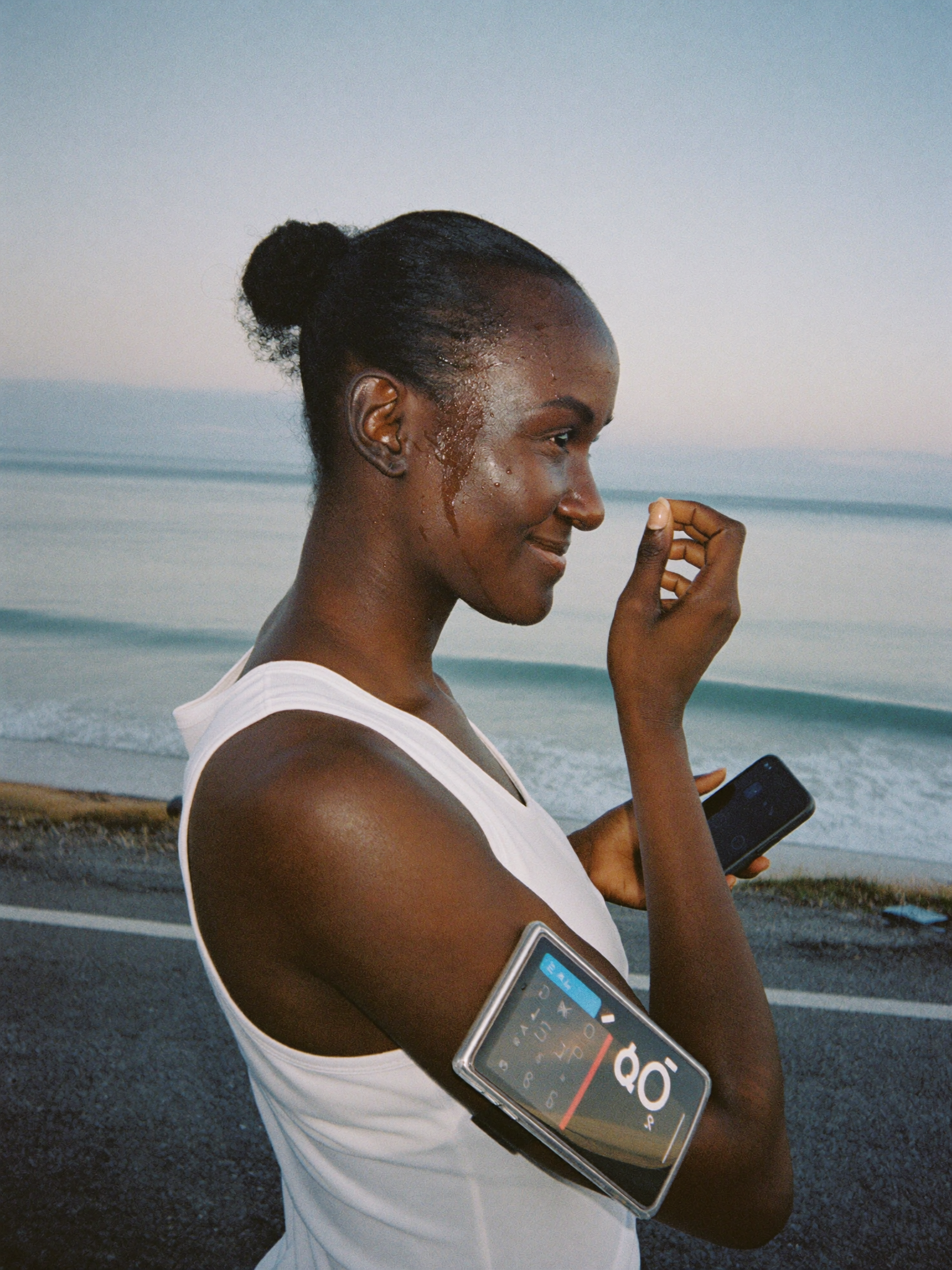 A runner pausing on a coastal road at dawn, catching her breath and looking out to sea.