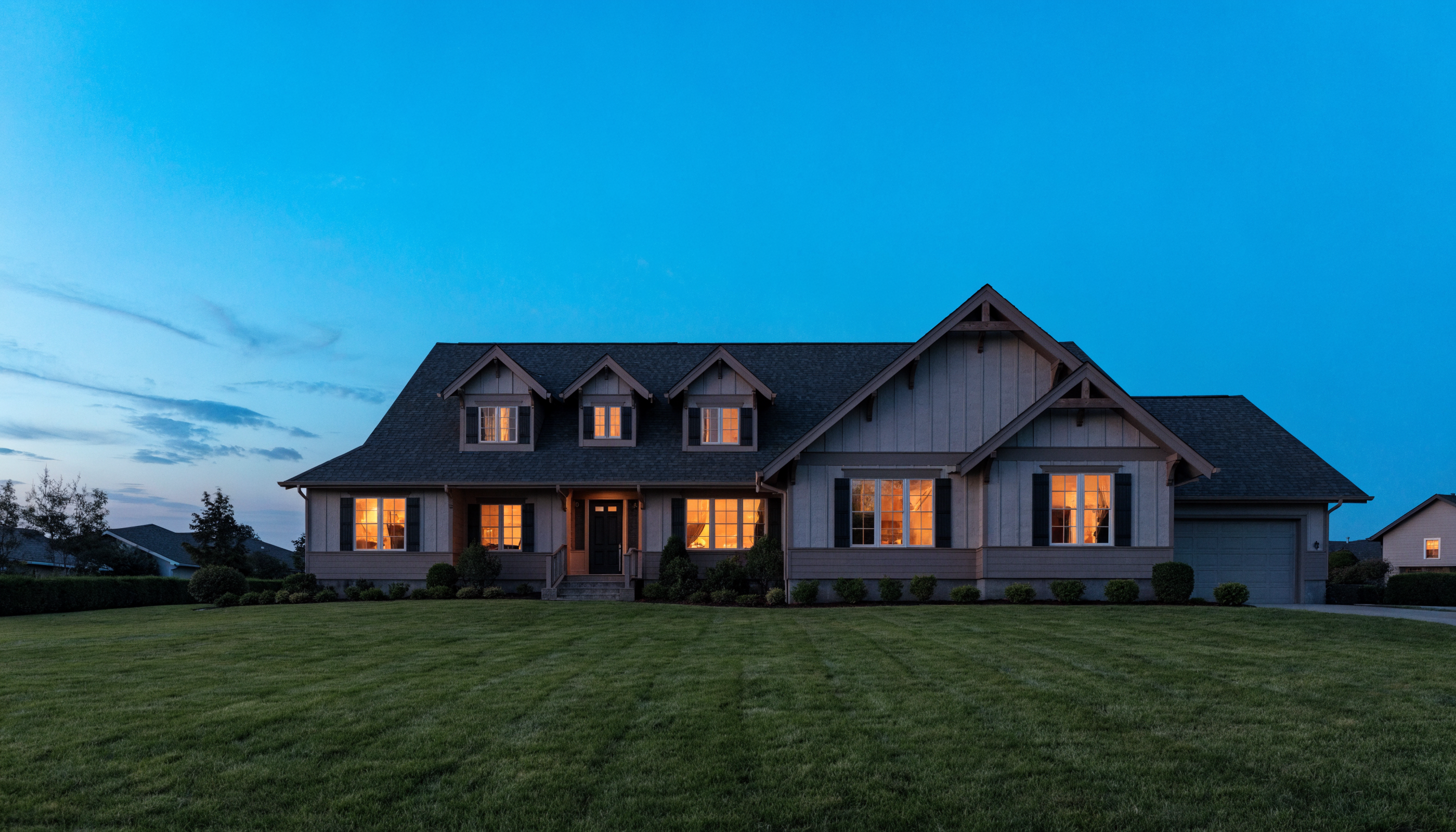 Upscale craftsman home at dusk with its steep roofline and lit attic dormer windows clearly visible