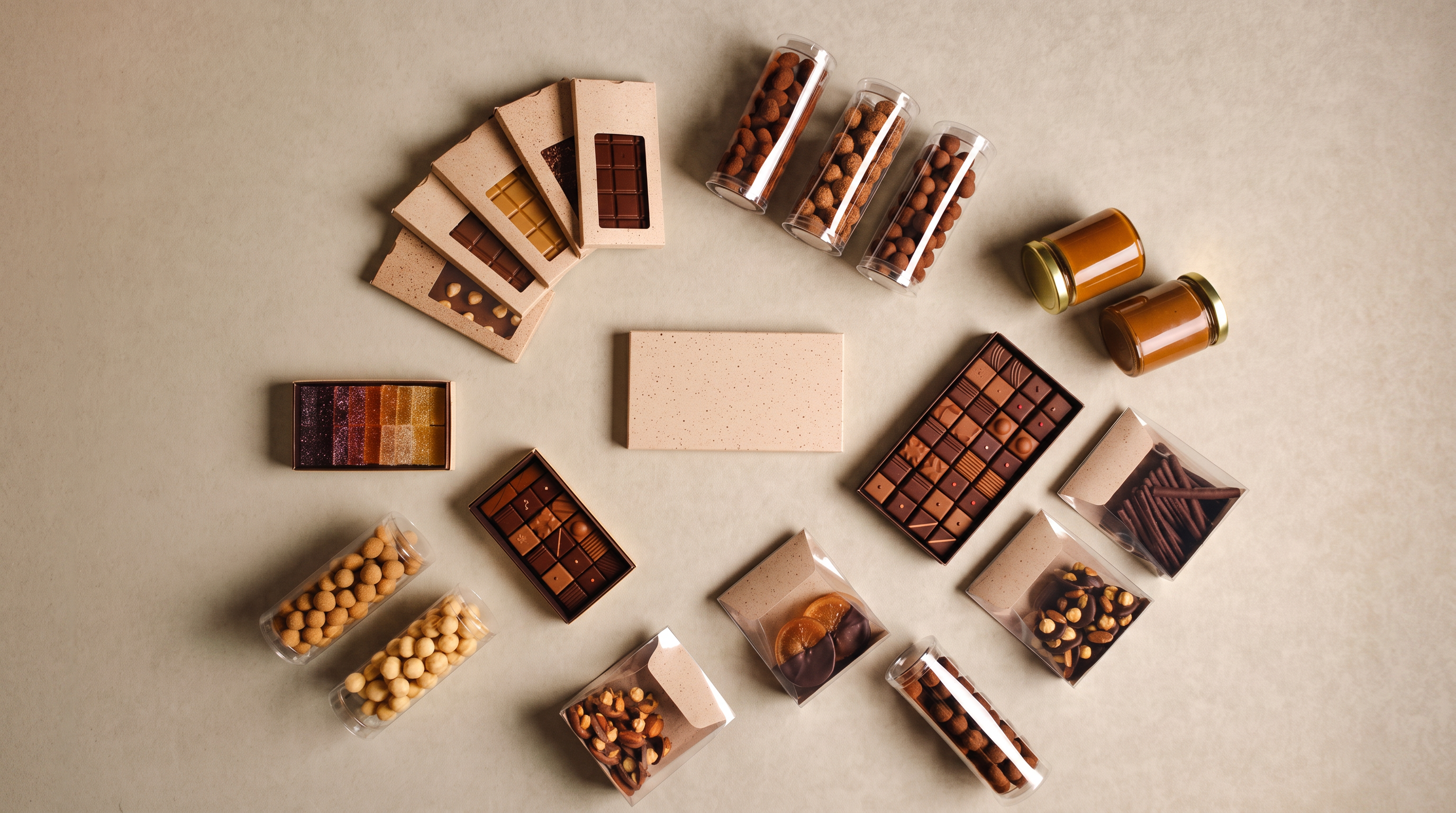 The Atelier Colette range laid out in a circle on warm putty paper — tablettes, bonbons, orangettes, hazelnuts and caramel spread