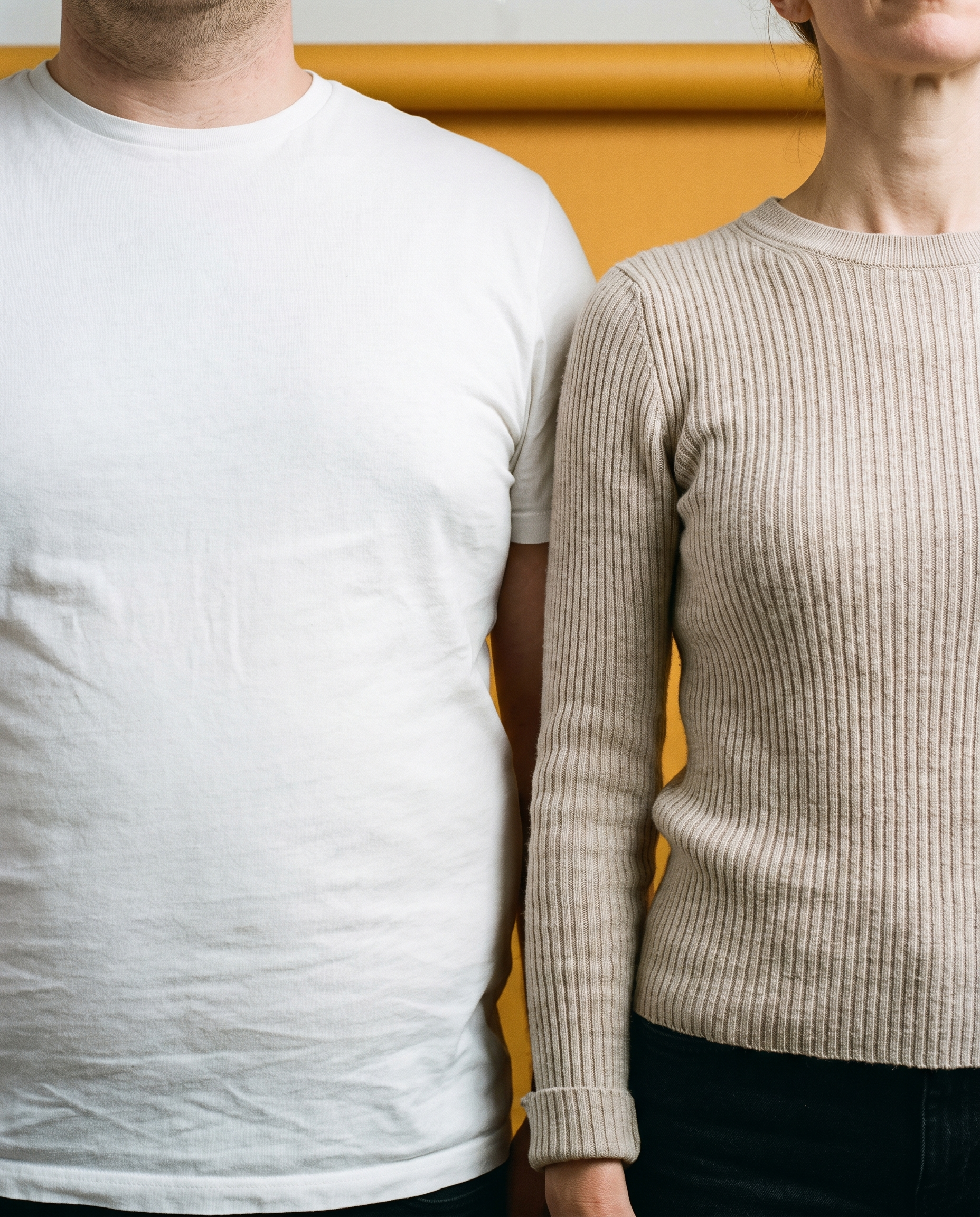 Two people of very different builds, cropped from collarbone to hip, on amber seamless