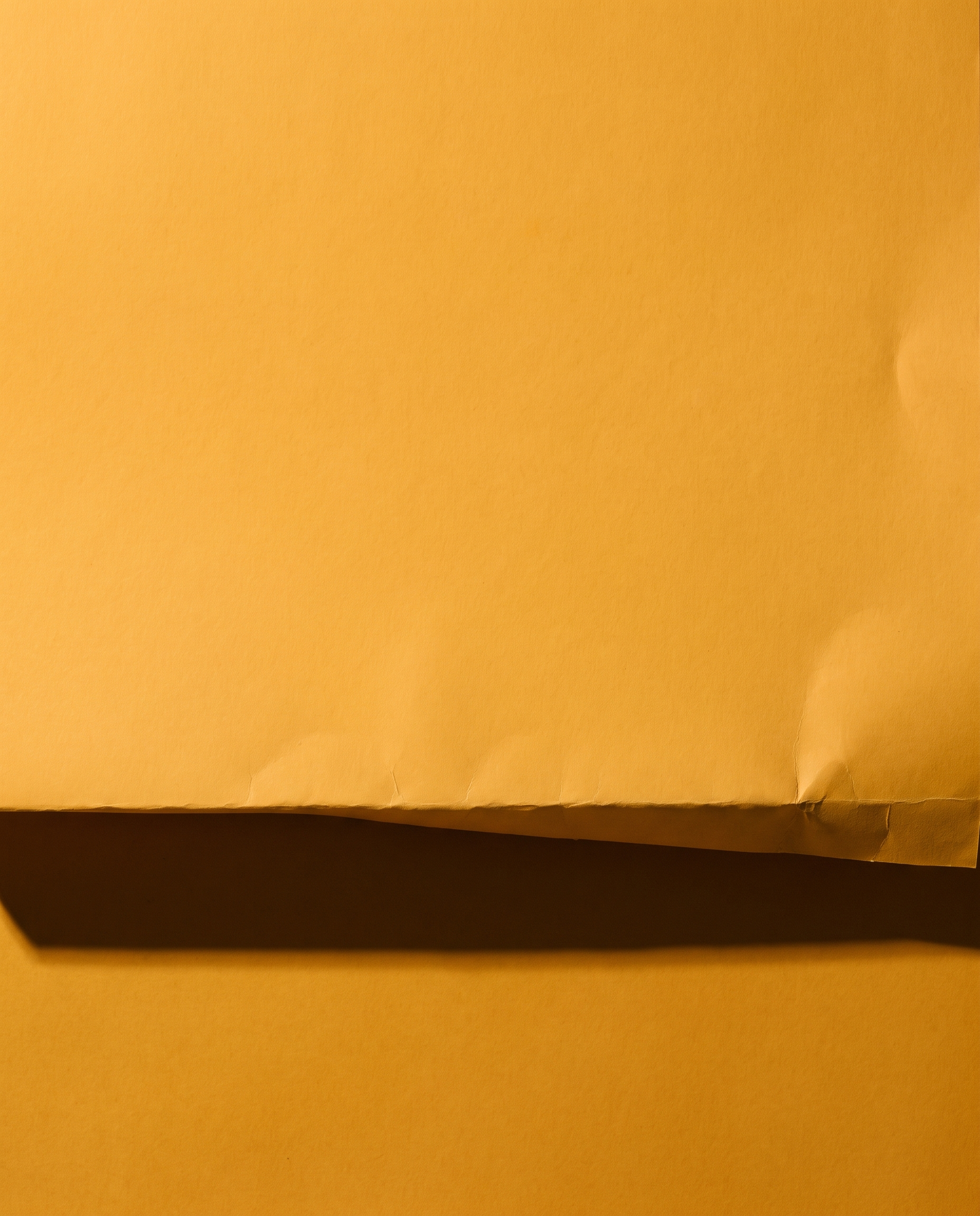 A sheet of amber paper folded into one hard ledge, throwing a long shadow